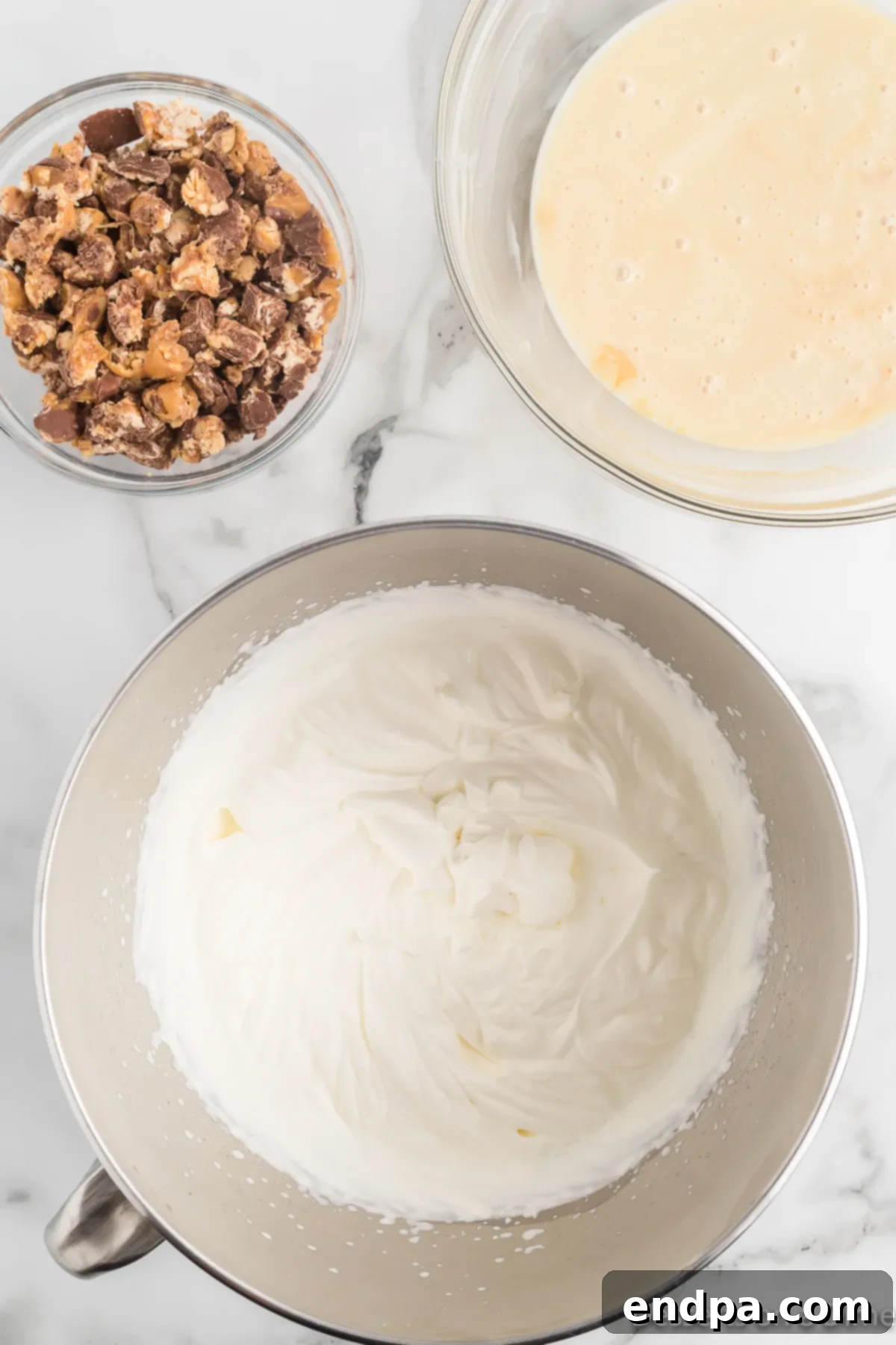 Decadent Homemade Snickers Ice Cream 6 A mixing bowl filled with heavy whipping cream that has been beaten to stiff peaks.