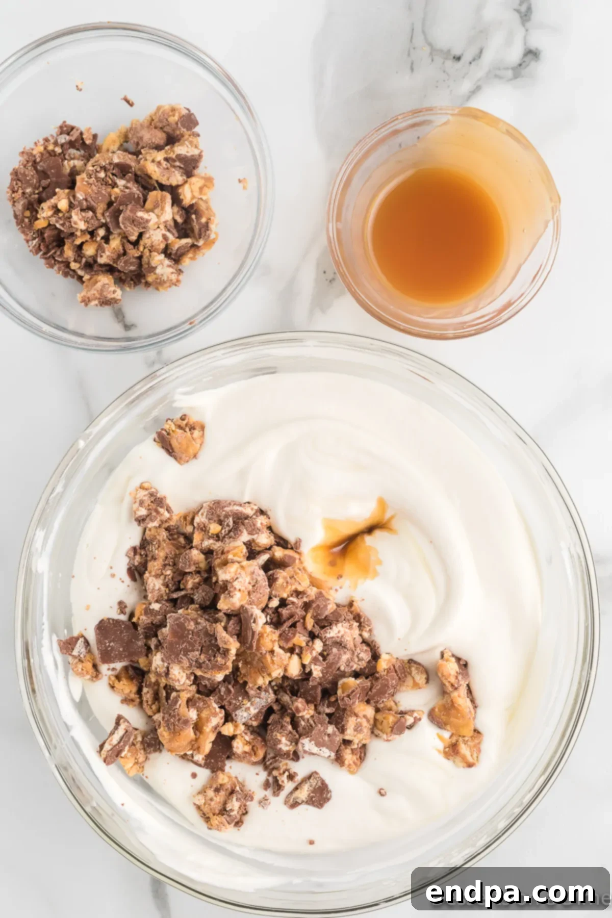 Decadent Homemade Snickers Ice Cream 8 Crushed candy bars and a swirl of caramel being folded into the ice cream base.