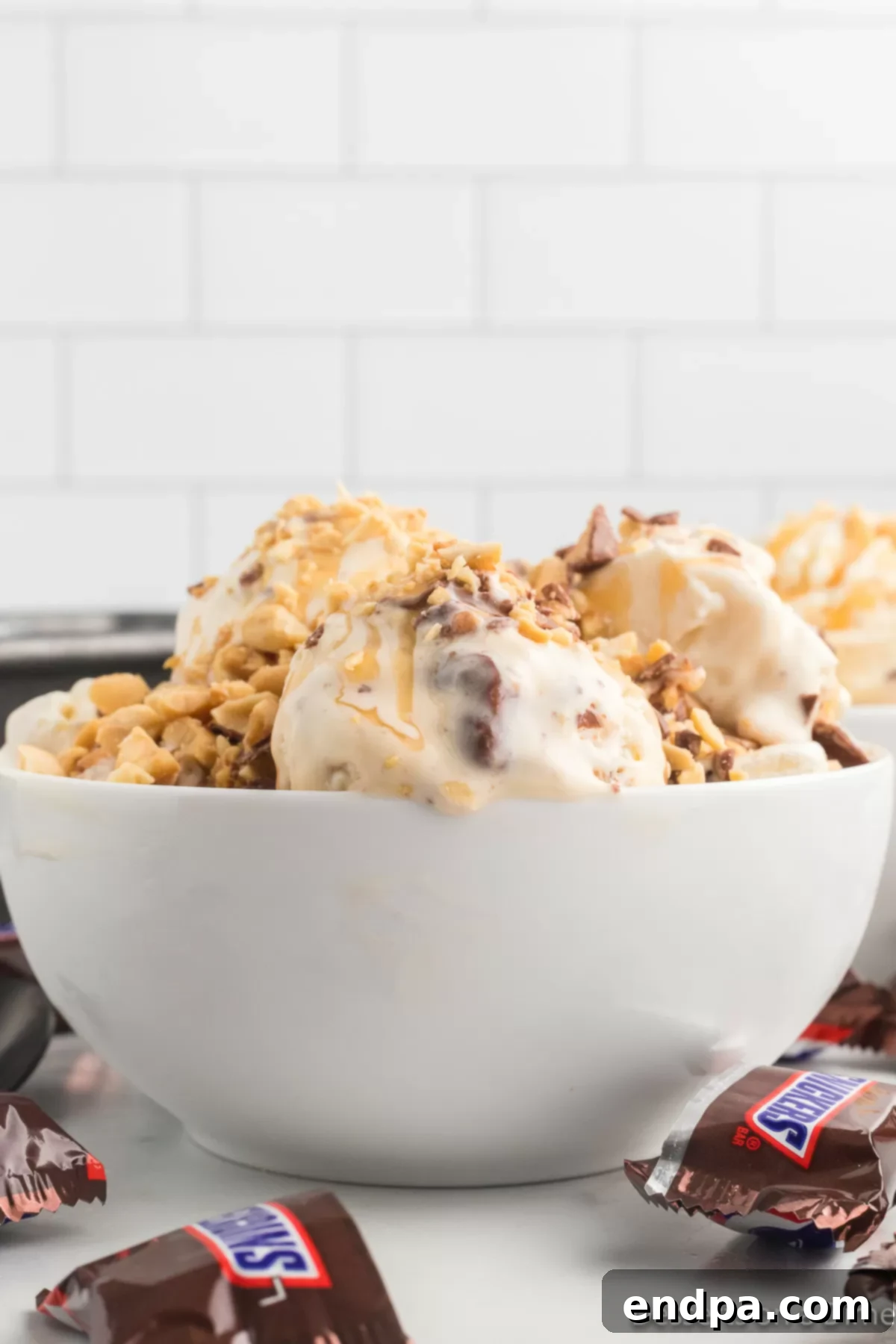 Decadent Homemade Snickers Ice Cream 10 A scoop of homemade Snickers ice cream in a white bowl, garnished with caramel drizzle and extra Snickers pieces.