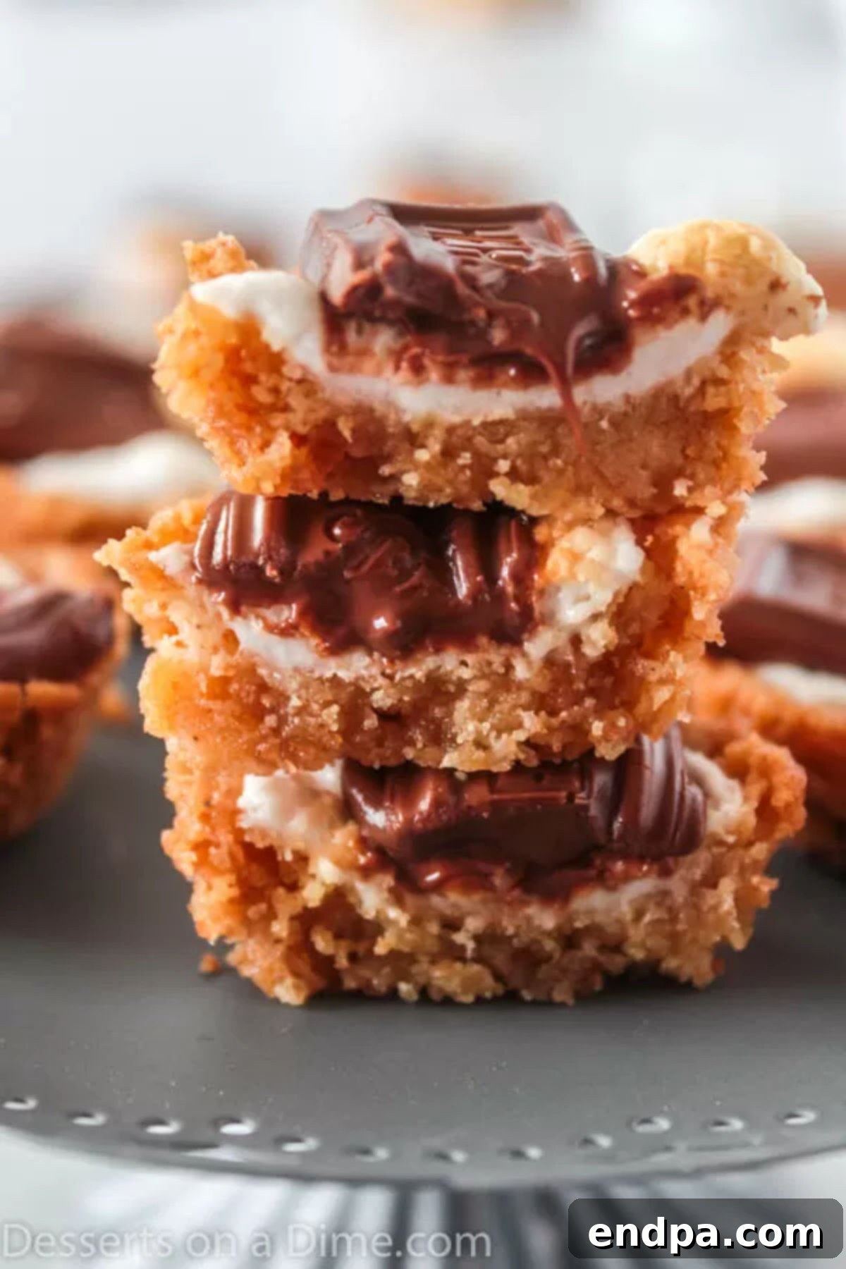 S'mores cookie cups are bite size treats with everything you love about s'mores. Make these mini s'mores bites with only 5 ingredients for a tasty recipe. Close up image of S'more cookies cups stacked on a white plate, showcasing their toasted marshmallows and melted chocolate.