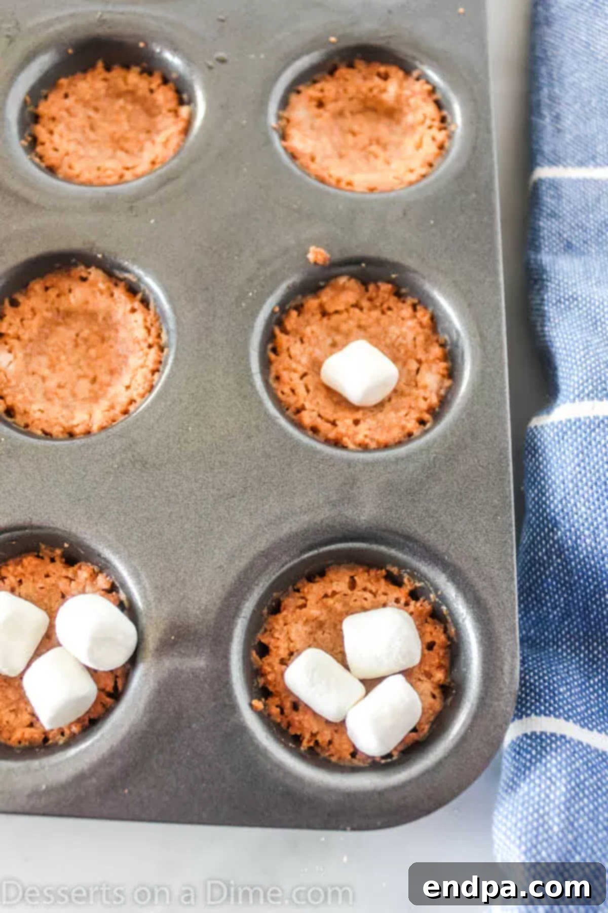 Gooey S'mores Cookie Bites 4 Baked graham cracker crusts in a mini muffin tin, each topped with several mini marshmallows.