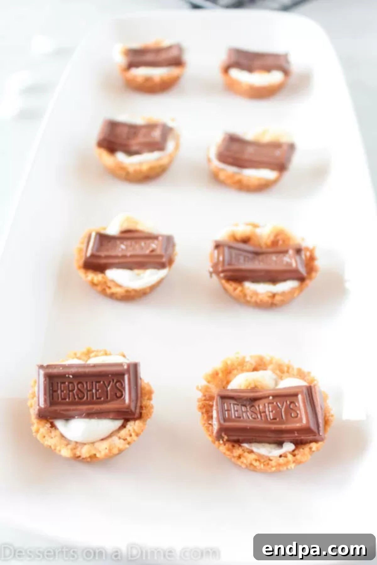 S'mores cookie cups are bite size treats with everything you love about s'mores. Make these mini s'mores bites with only 5 ingredients for a tasty recipe. Close up image of mini s'more cookie cups arranged neatly on a white platter, ready to be served.