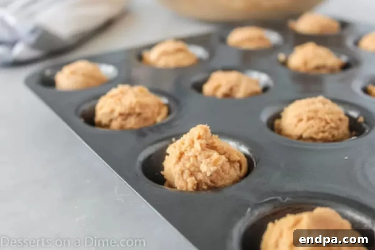 Cookie dough balls placed in a greased mini muffin pan, ready for baking.
