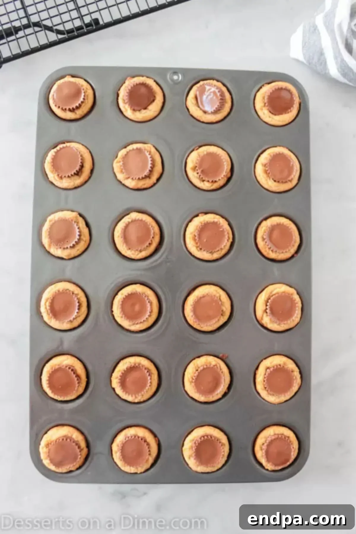 Freshly baked cookies in a muffin tin, topped with mini Reese's peanut butter cups pressed into their centers.
