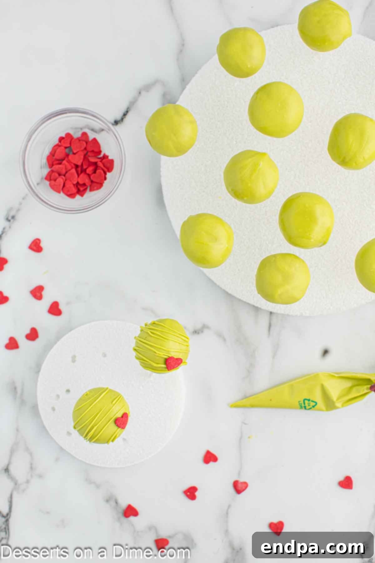 Grinchmas Cake Pops 11 A Grinch Cake Pop being decorated with a red candy heart and drizzled with candy melts.