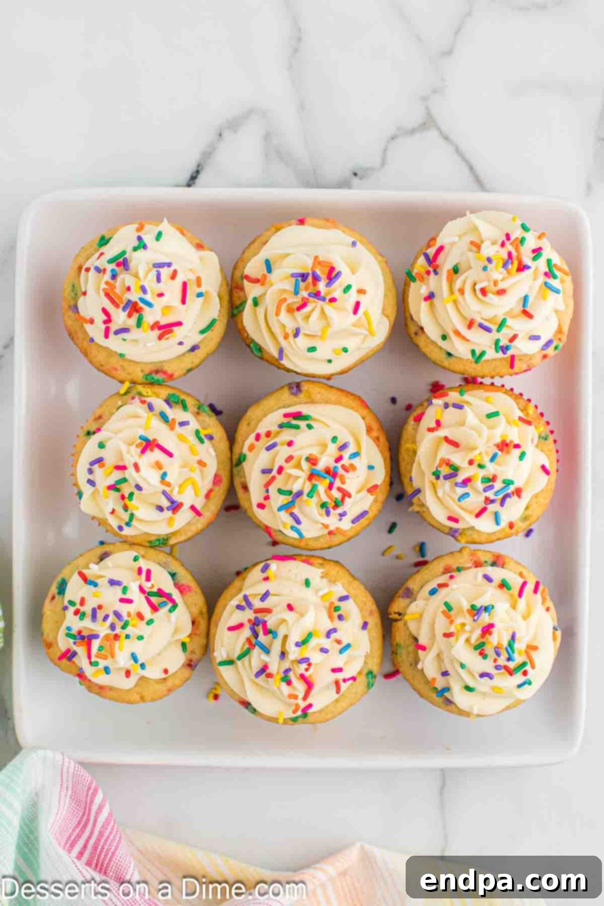 Confetti cupcake being frosted with vanilla buttercream using a piping bag and star tip.