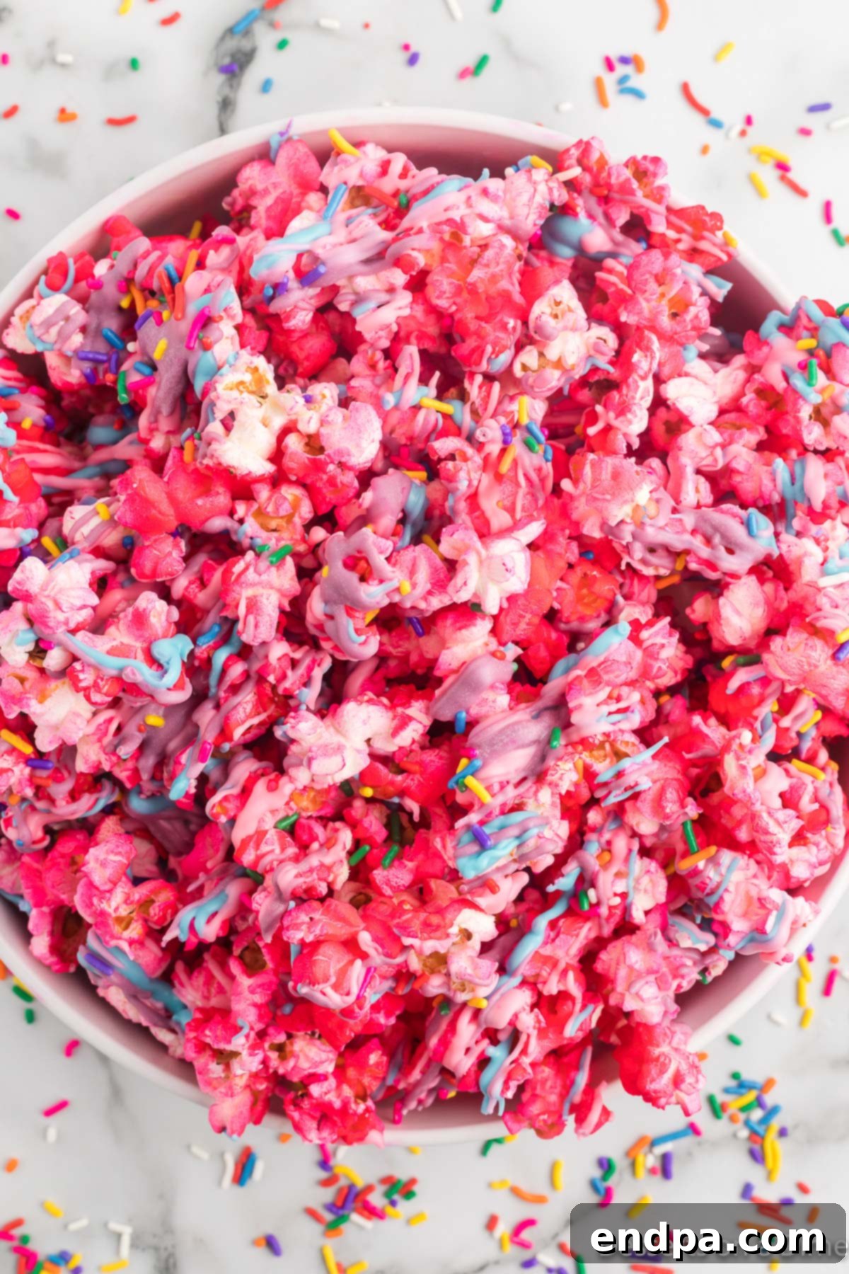 A large bowl filled with vibrant, multicolored Unicorn Popcorn, generously coated in pink, blue, and purple candy melts and sparkling with rainbow sprinkles. It's a visually stunning, fun, and festive treat, ready for any party.