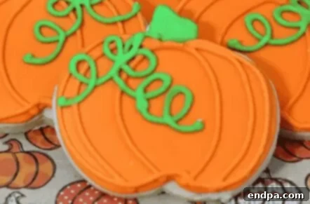 Pumpkin-shaped sugar cookies decorated with orange frosting and green stems.