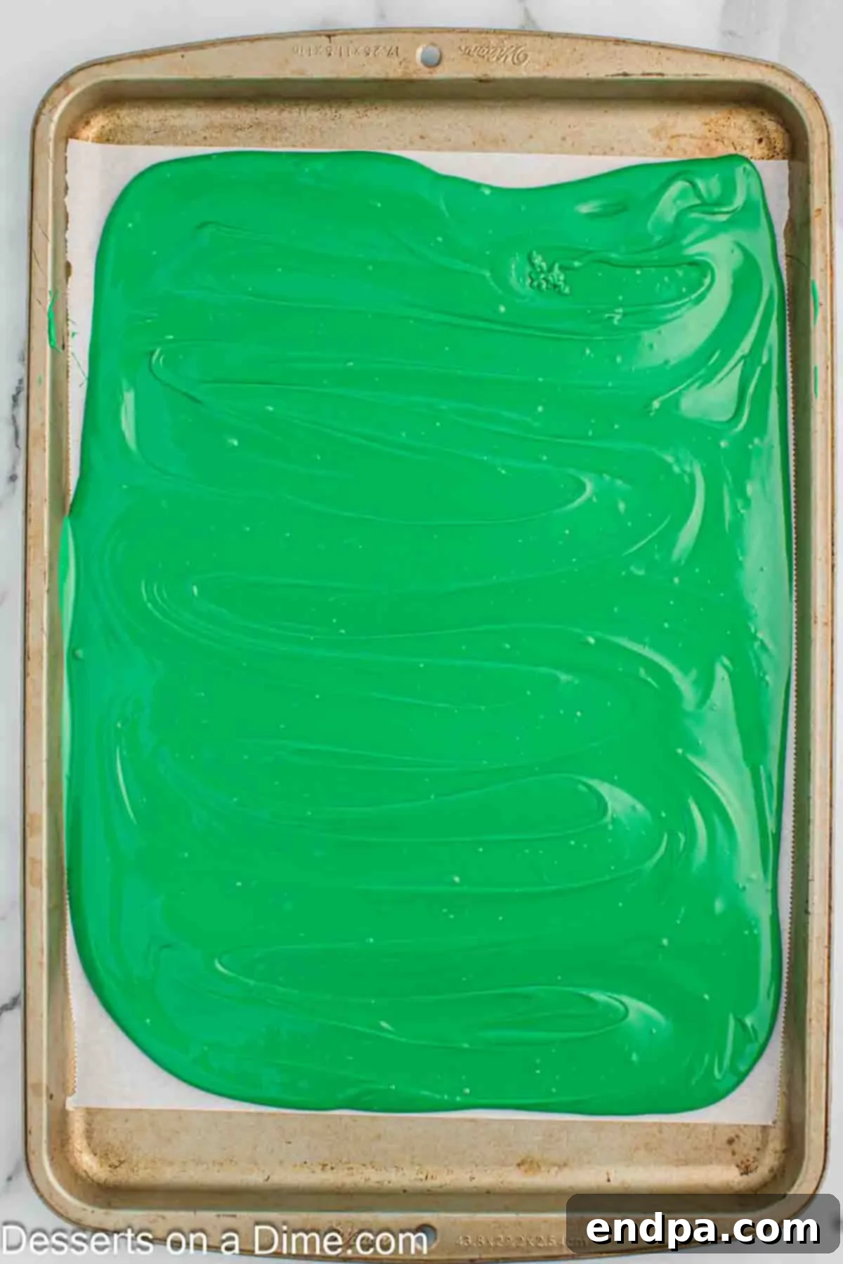 Spreading the vibrant green melted candy melts evenly onto a parchment-lined baking sheet.