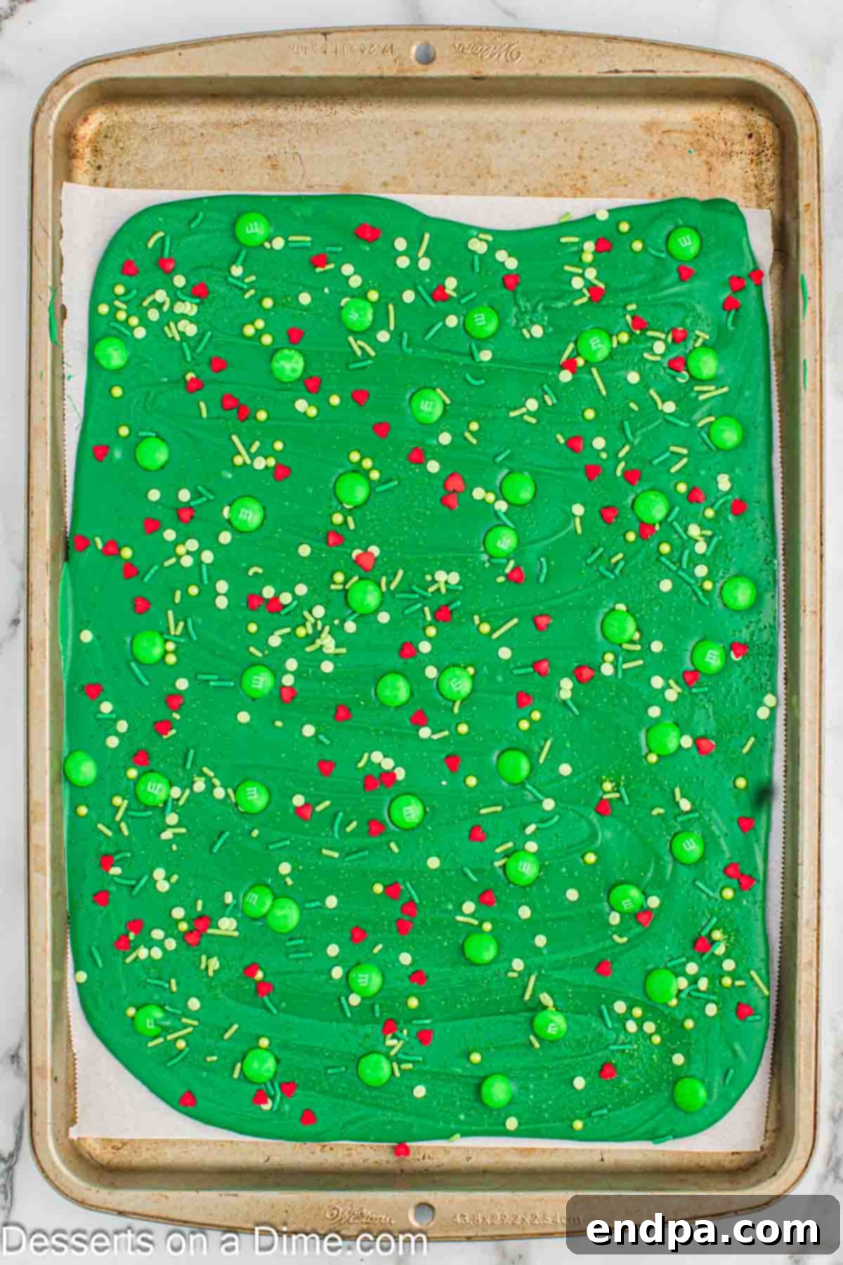 Topping the freshly spread green melted candy with green M&Ms, green sprinkles, and red candy hearts.