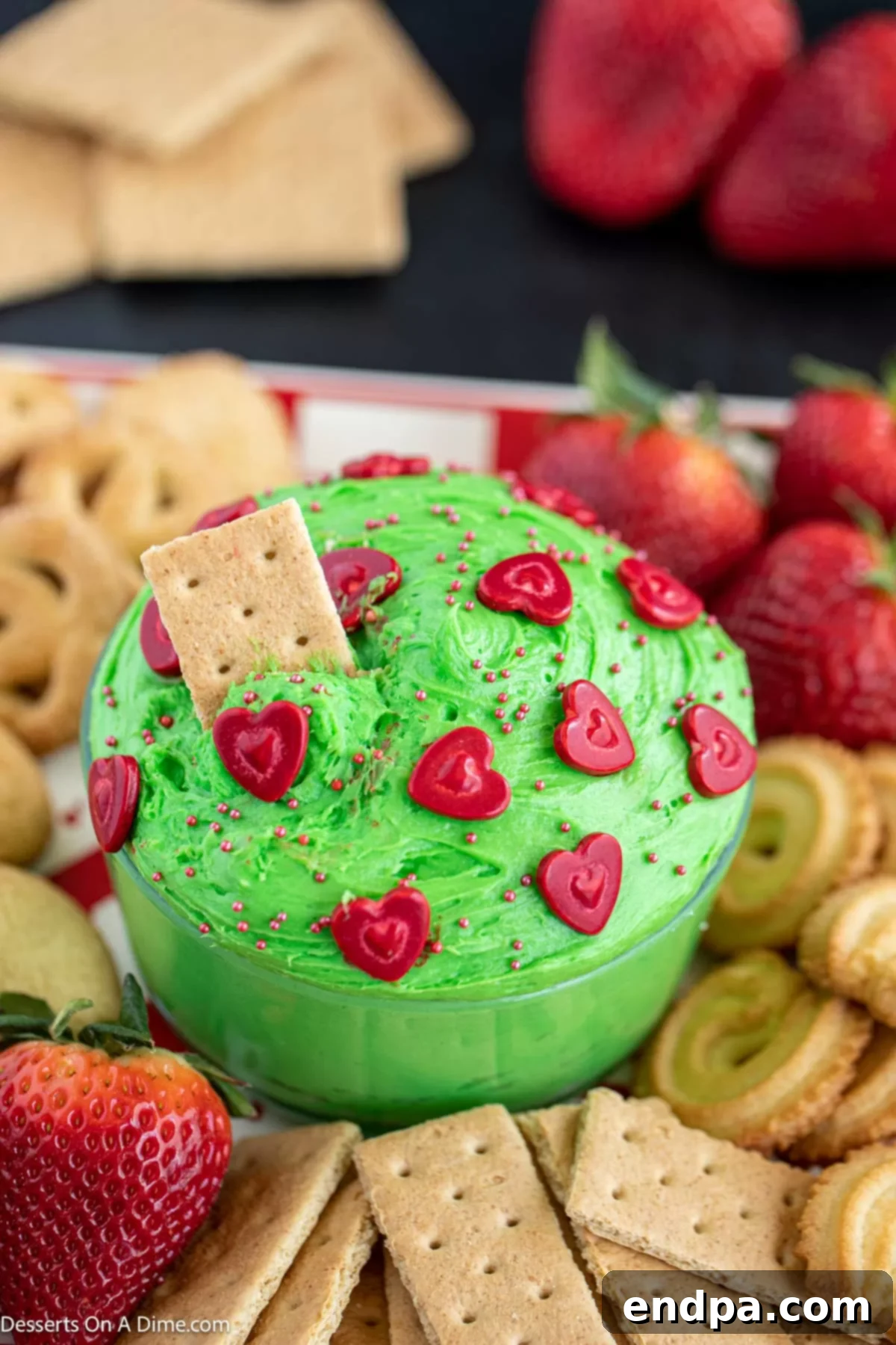 Heart-Growing Grinch Dip 8 Grinch dip in a bowl with a graham cracker stuck inside, ready to be enjoyed.