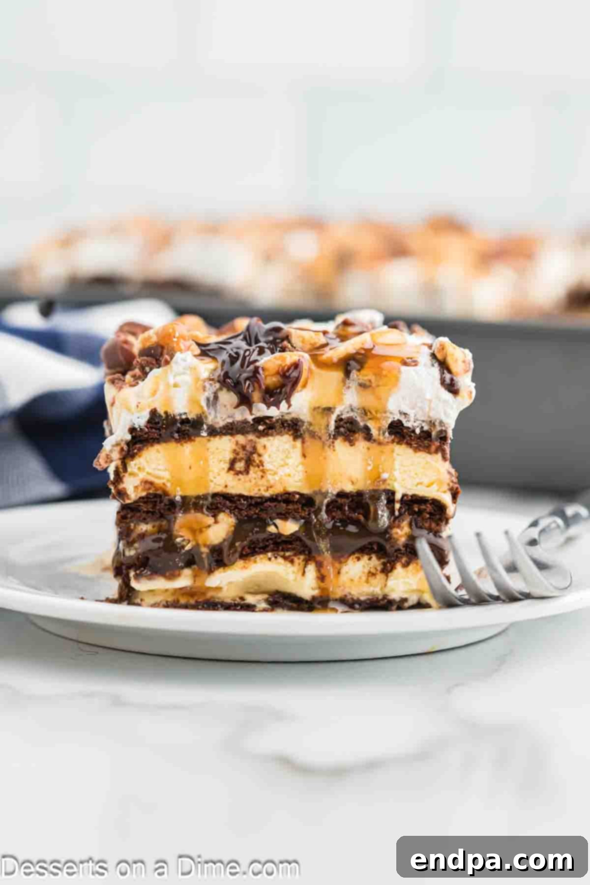 Ultimate Snickers Ice Cream Cake 13 A perfectly cut slice of Snickers Ice Cream Cake on a white plate, revealing its detailed layers of ice cream, chocolate, caramel, Snickers, and whipped topping, ready to be enjoyed.