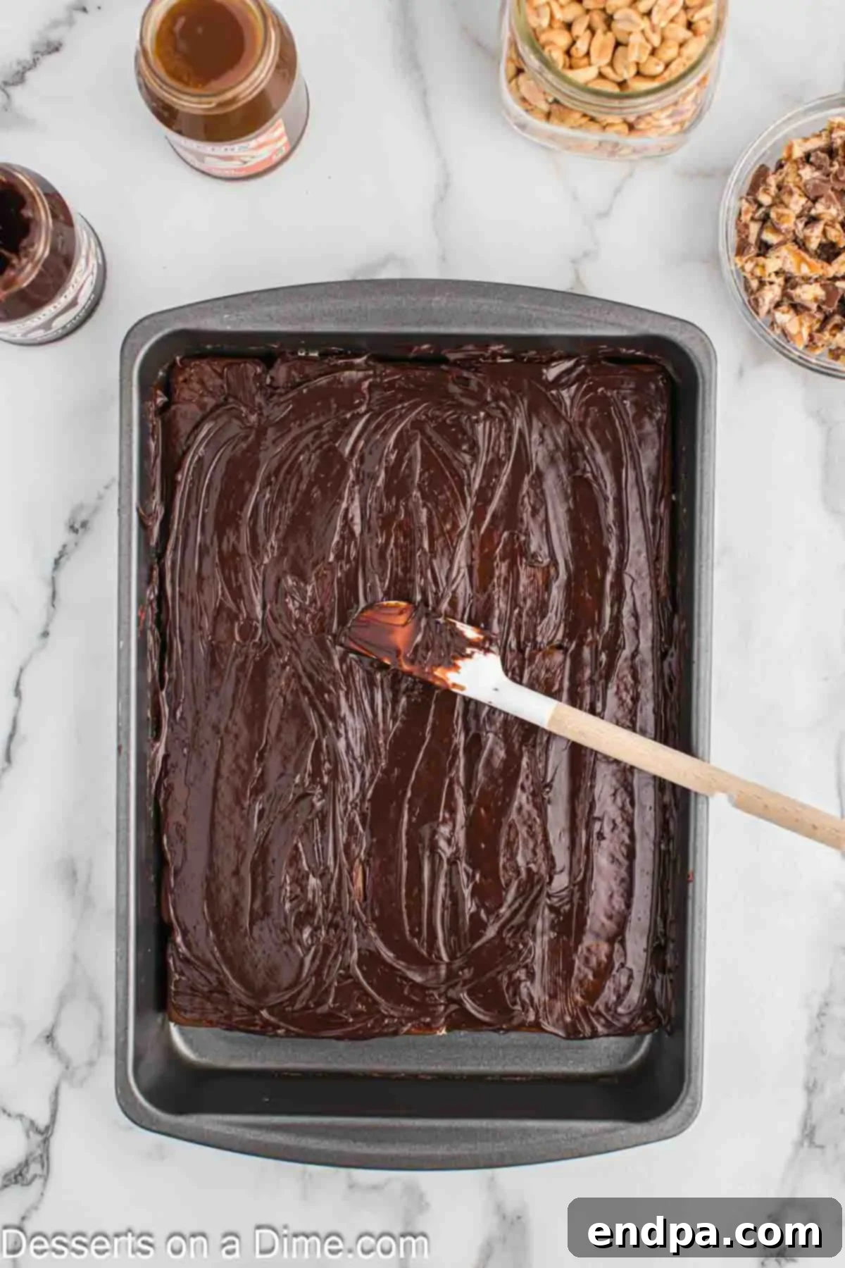 Ultimate Snickers Ice Cream Cake 5 A layer of warm hot fudge sauce being spread evenly over the ice cream sandwiches, creating a rich chocolate foundation.