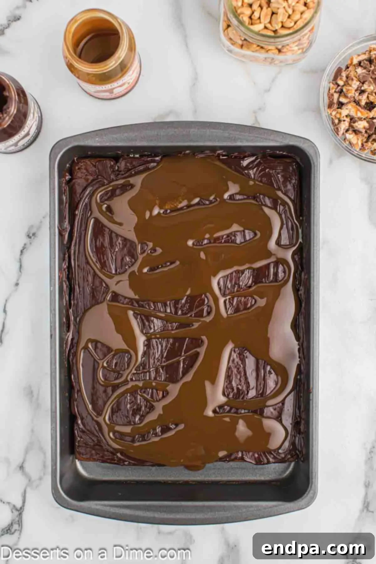 Ultimate Snickers Ice Cream Cake 6 Caramel sauce drizzled over the hot fudge layer, followed by a sprinkle of chopped Snickers bars and roasted peanuts, ready for the next layer.