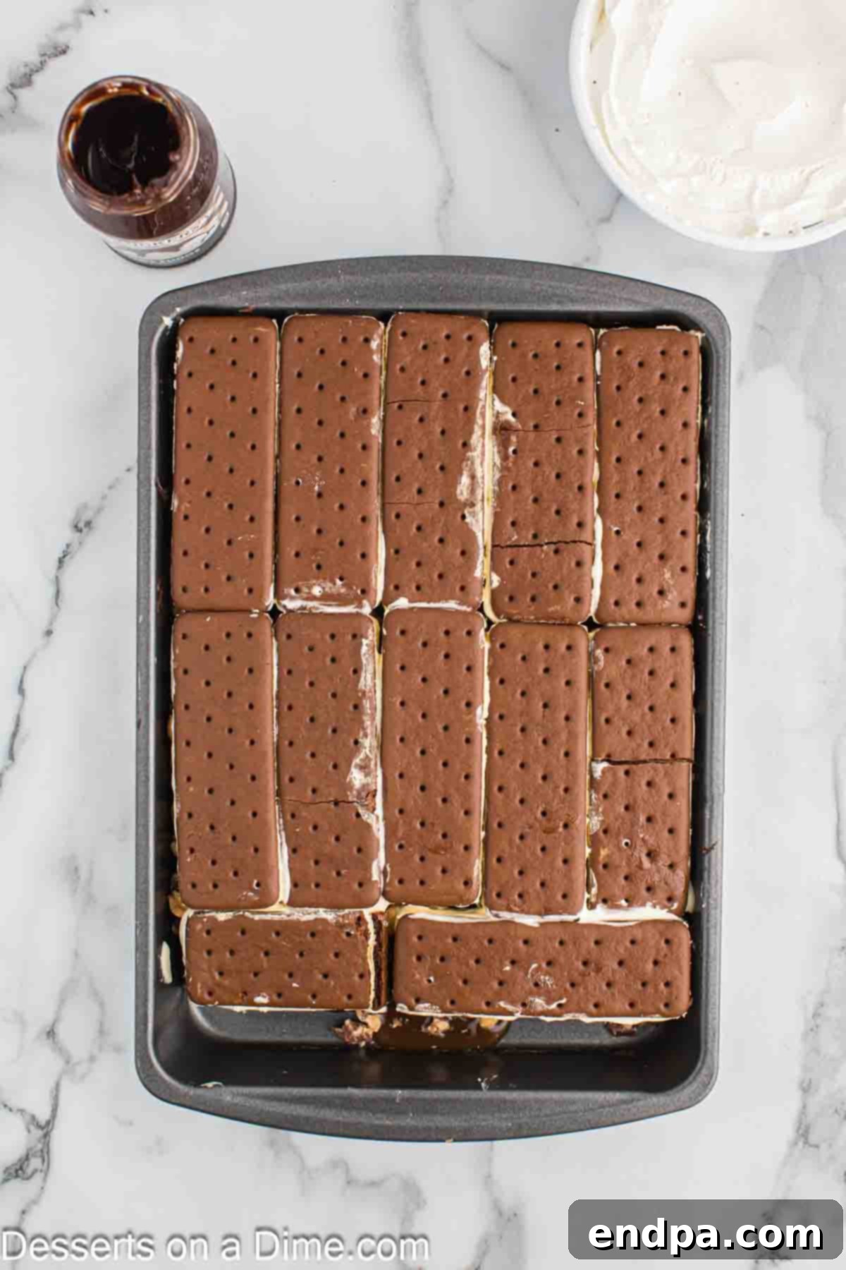 Ultimate Snickers Ice Cream Cake 7 The second layer of ice cream sandwiches being carefully placed on top of the caramel, peanuts, and Snickers, completing the sandwich base.