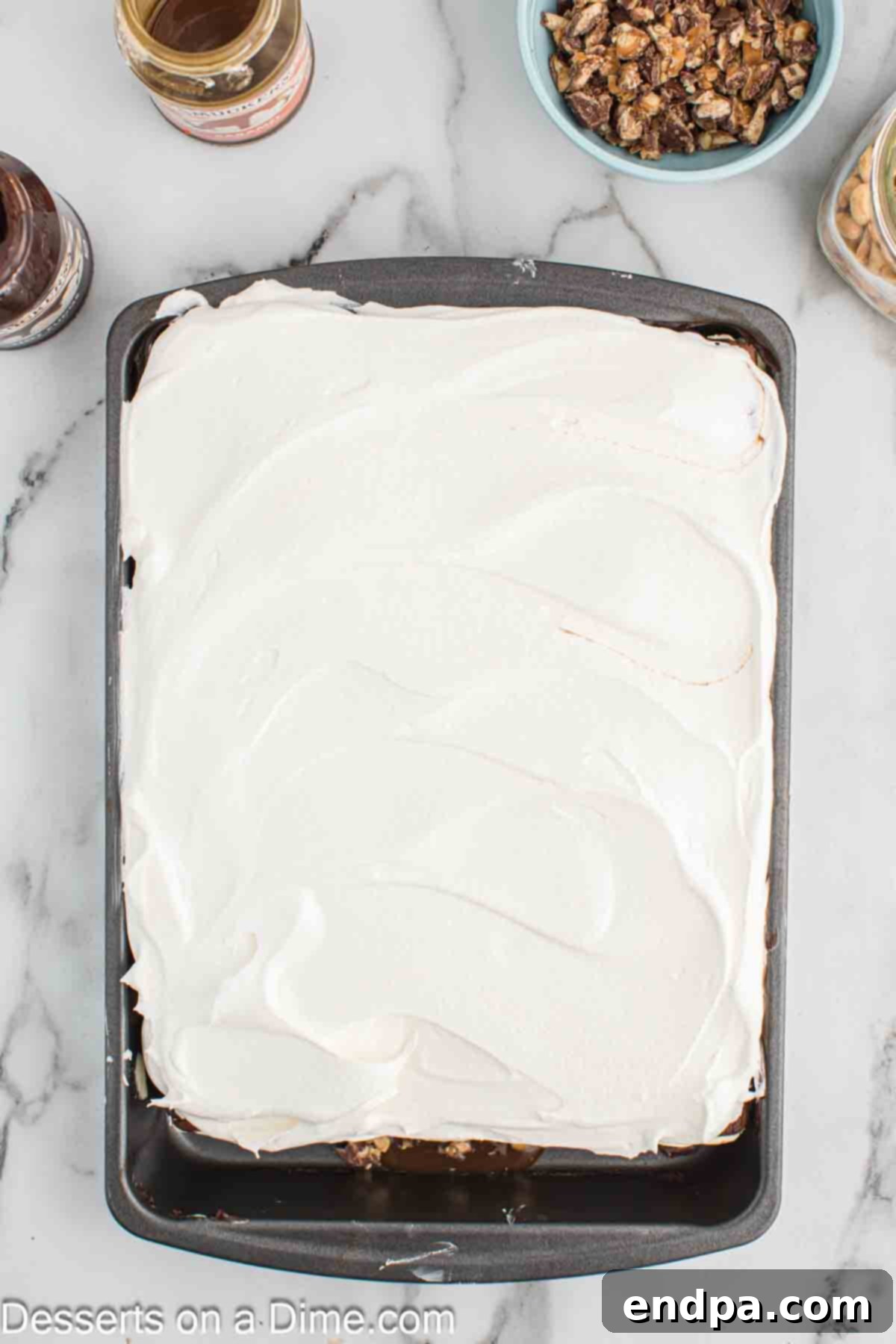 Ultimate Snickers Ice Cream Cake 9 A thick, fluffy layer of whipped topping spread over the final hot fudge layer, creating a soft, appealing top for the Snickers ice cream cake.