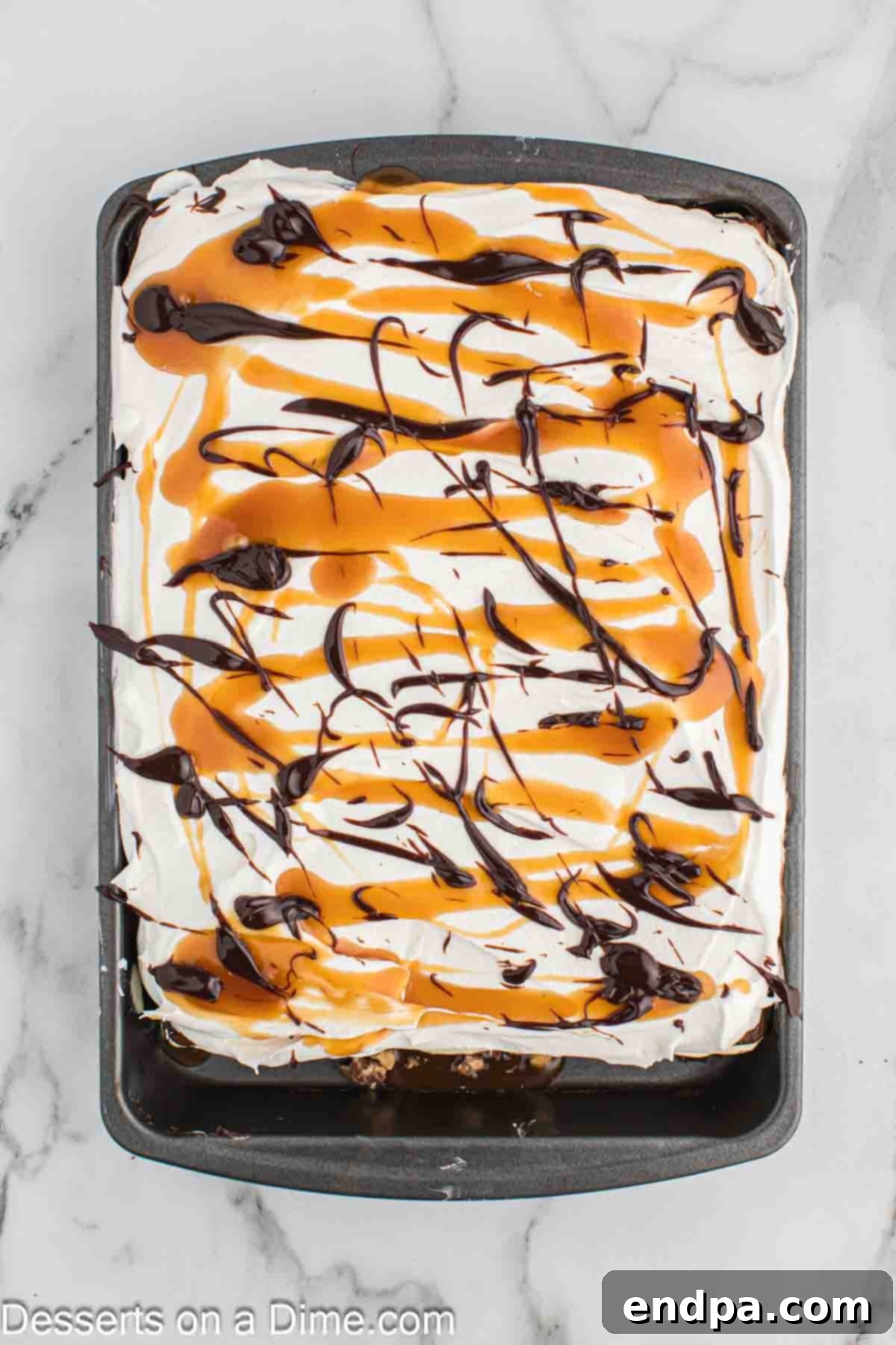 Ultimate Snickers Ice Cream Cake 10 Finished Snickers ice cream cake, beautifully garnished with drizzles of caramel and hot fudge, and a sprinkle of chopped Snickers and peanuts, ready for freezing.