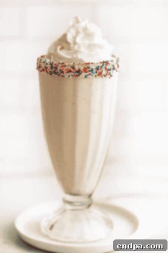 A tall glass of creamy vanilla milkshake topped with whipped cream.