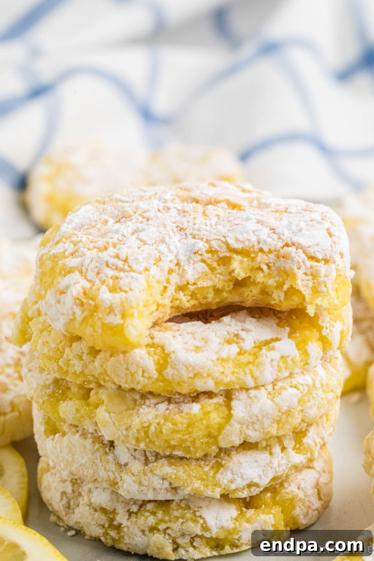 Lemon cookies stacked in a pyramid on a white background, highlighting their powdered sugar coating and vibrant color.