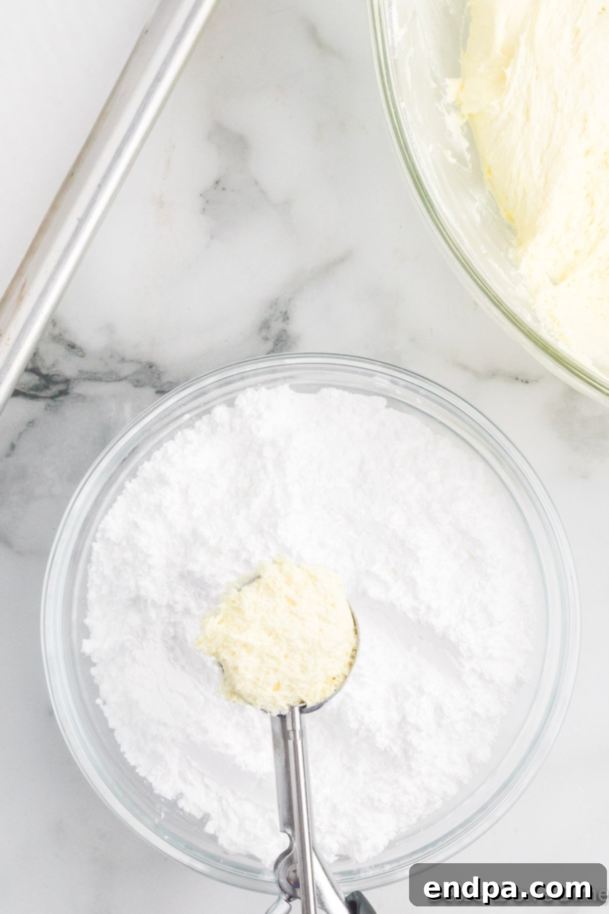 Rounded cookie dough balls are being dipped and coated in powdered sugar.