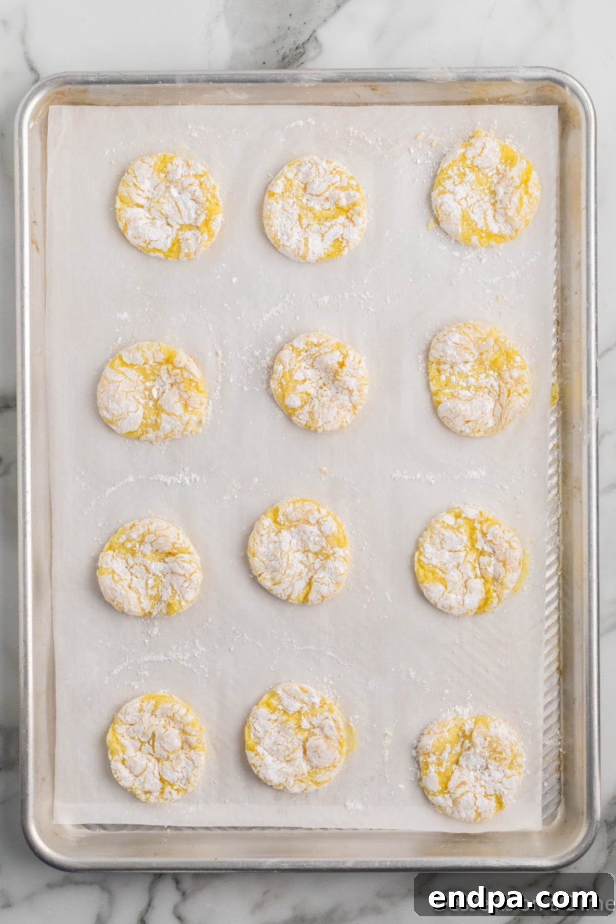 Powdered sugar-coated lemon cookie dough balls arranged on a baking sheet, ready for the oven.