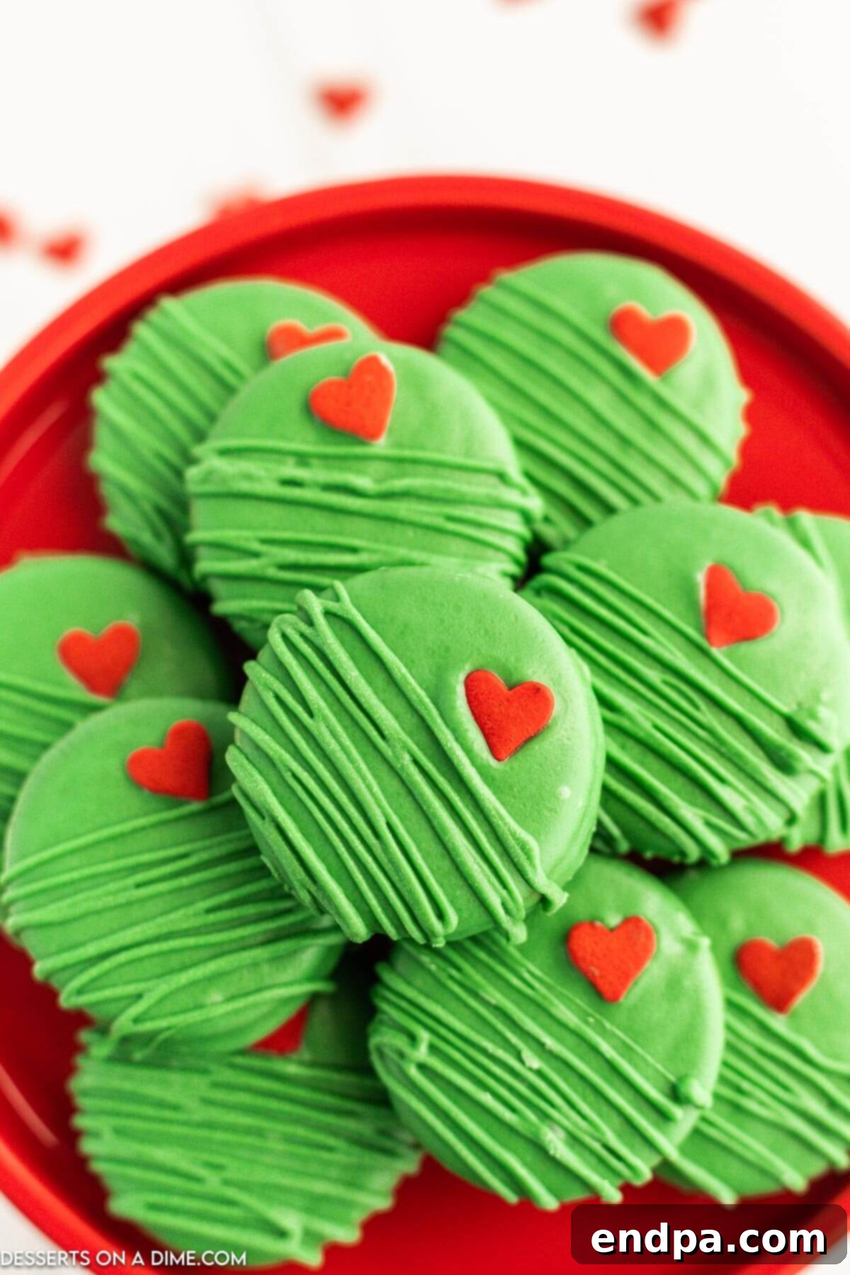 The Grinch's Heart-Melting Oreos 2 A festive platter of green Grinch Chocolate Covered Oreos, each topped with a small red heart sprinkle, perfect for a holiday party.