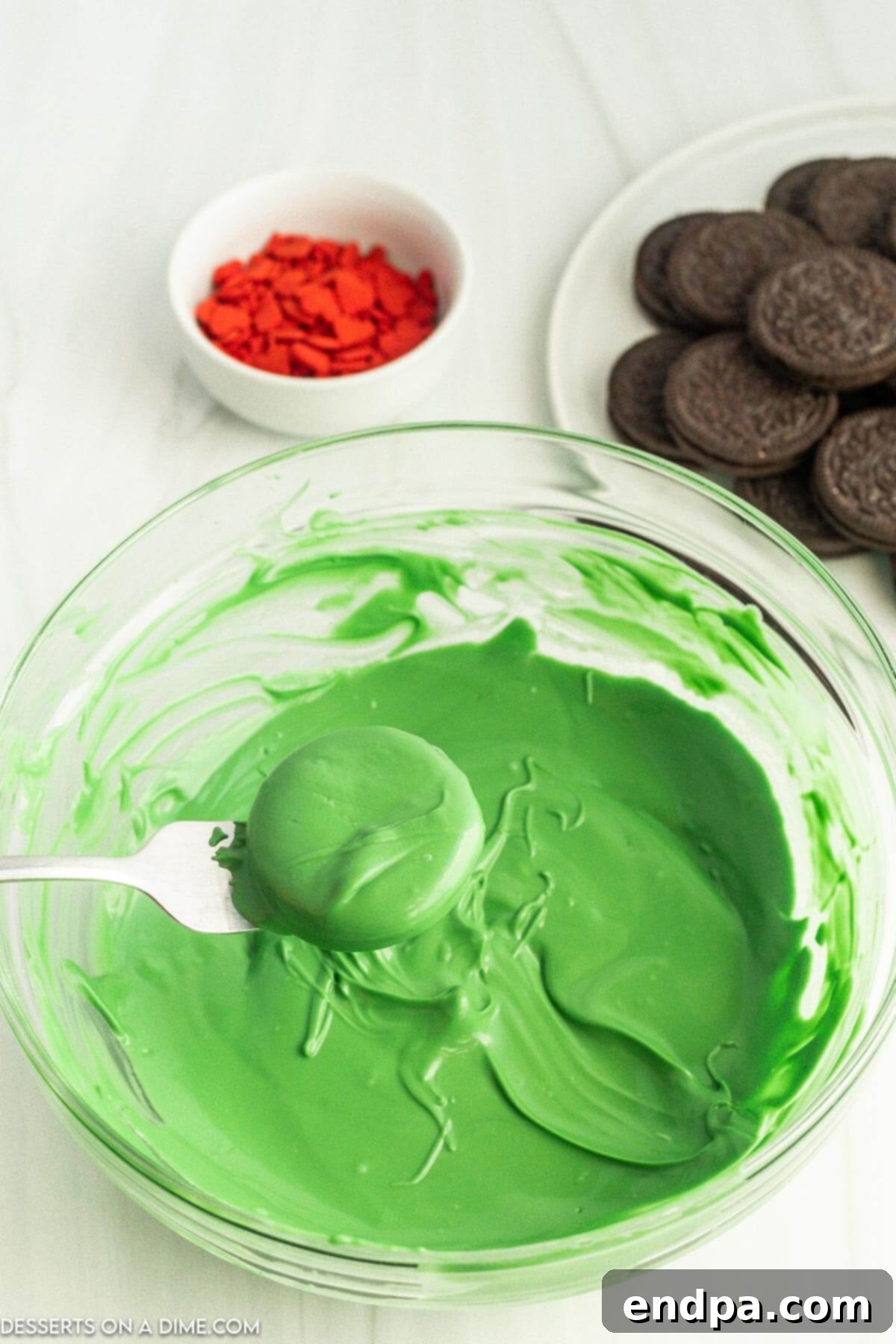 The Grinch's Heart-Melting Oreos 5 An Oreo cookie being carefully dipped into the vibrant green melted candy coating using a fork.