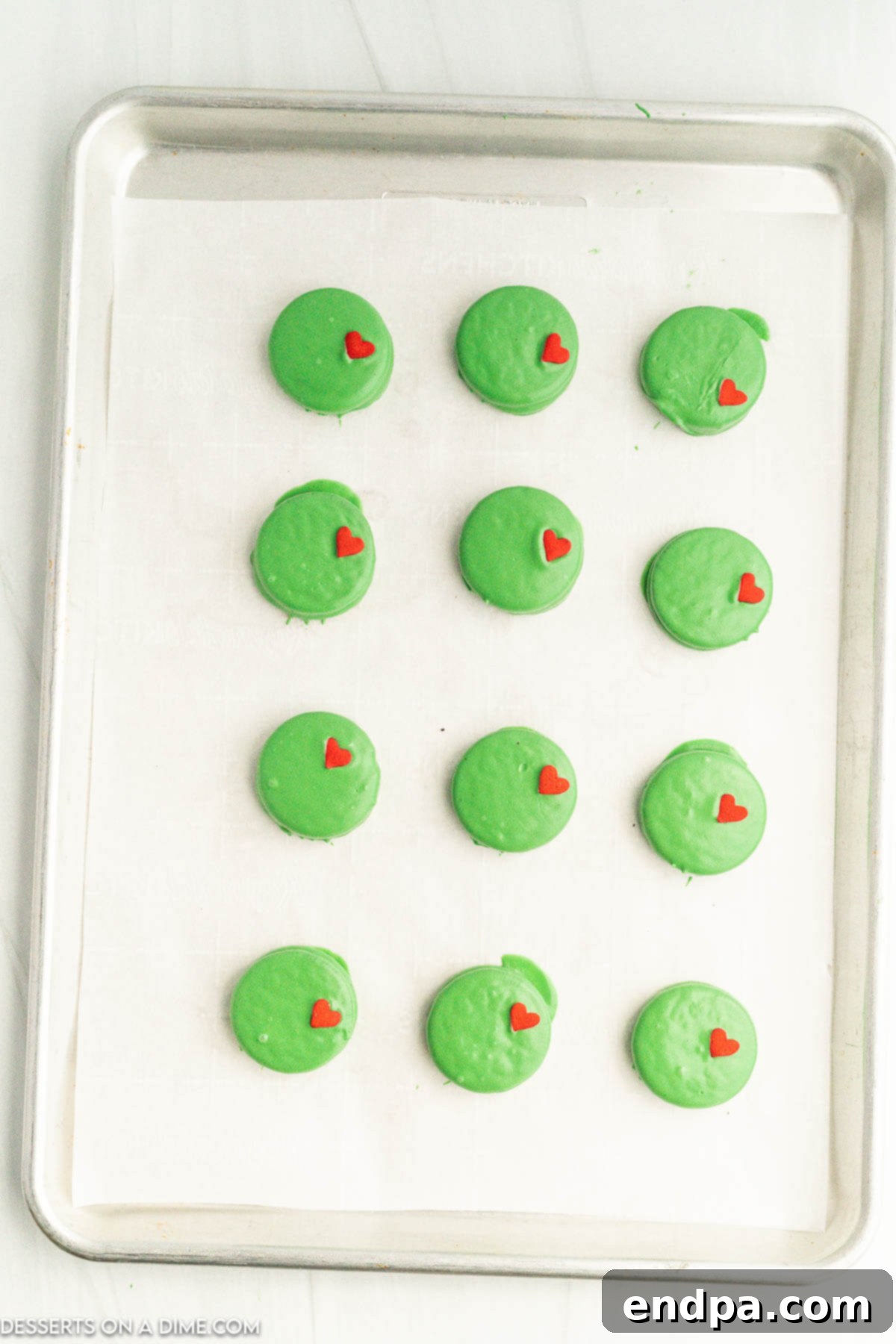 The Grinch's Heart-Melting Oreos 6 Several green-coated Oreo cookies arranged on a lined baking sheet, before adding sprinkles.