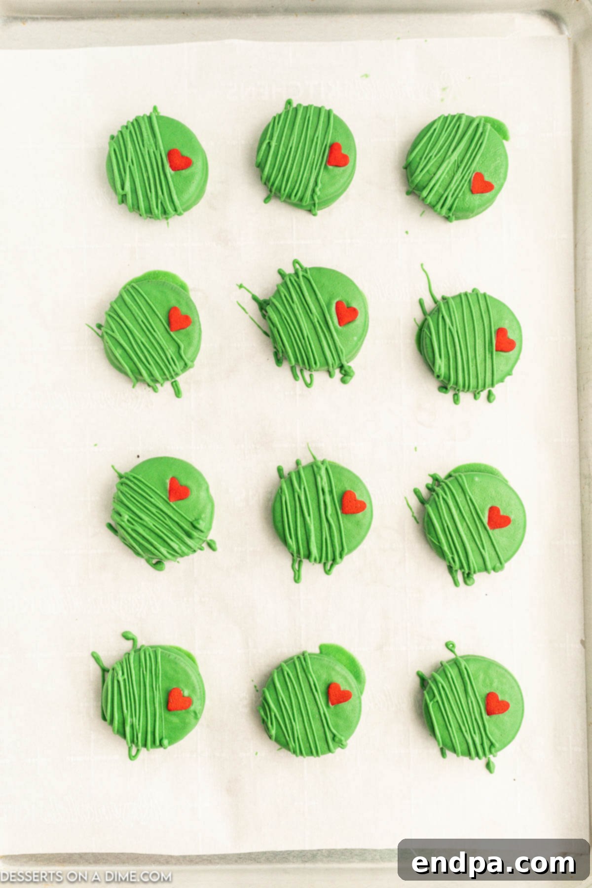 The Grinch's Heart-Melting Oreos 7 Green-coated Oreo cookies on a baking sheet, now adorned with red heart sprinkles, setting at room temperature.