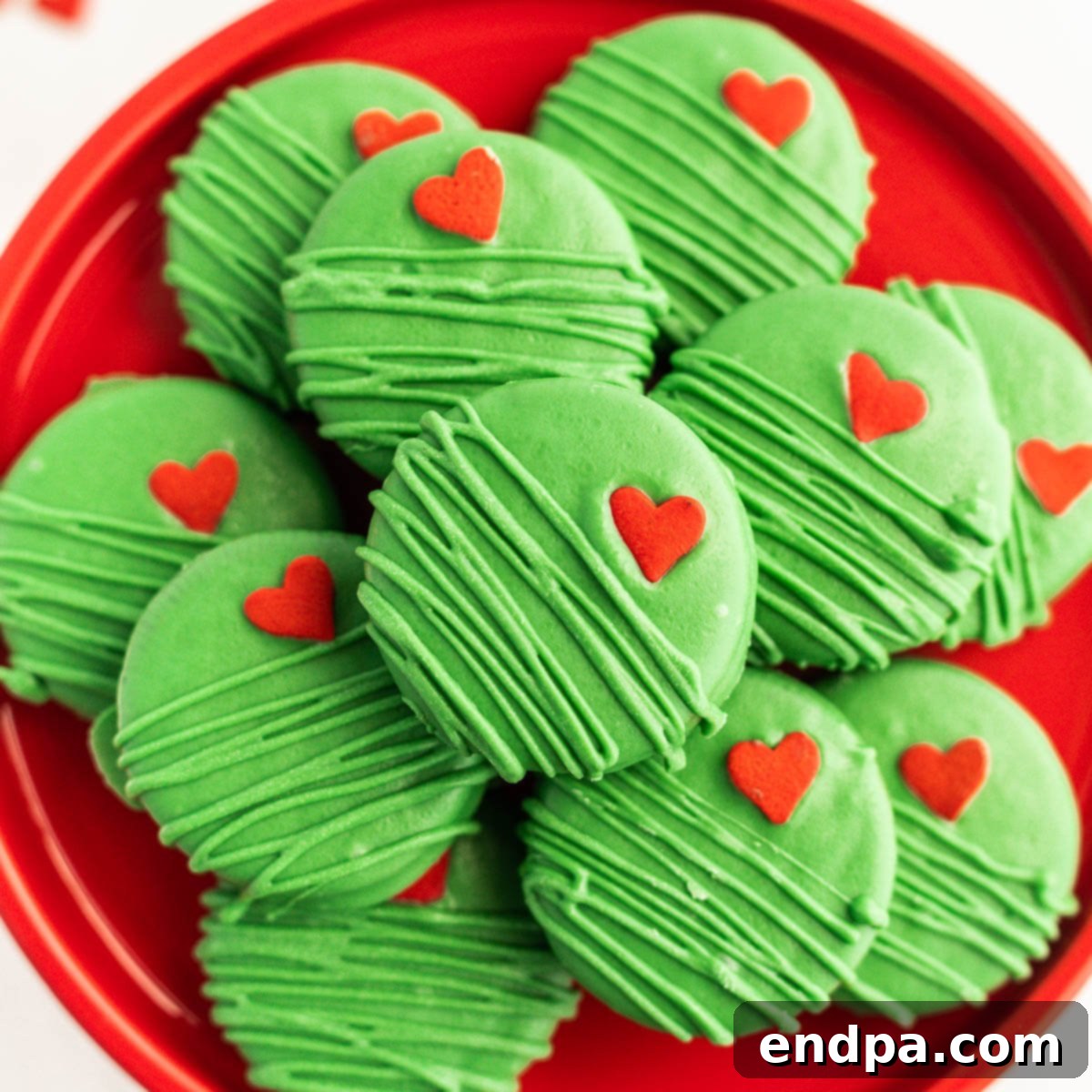 The Grinch's Heart-Melting Oreos 9 Finished Grinch Chocolate Covered Oreos on a festive platter, with a red heart on each green cookie.