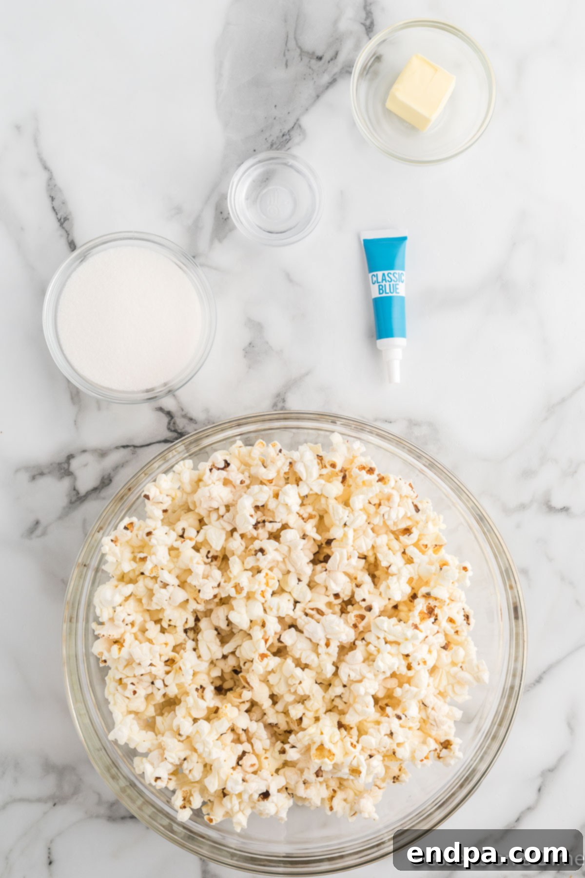 Ingredients laid out for making Candy Popcorn, including popped popcorn, granulated sugar, butter, and food coloring.