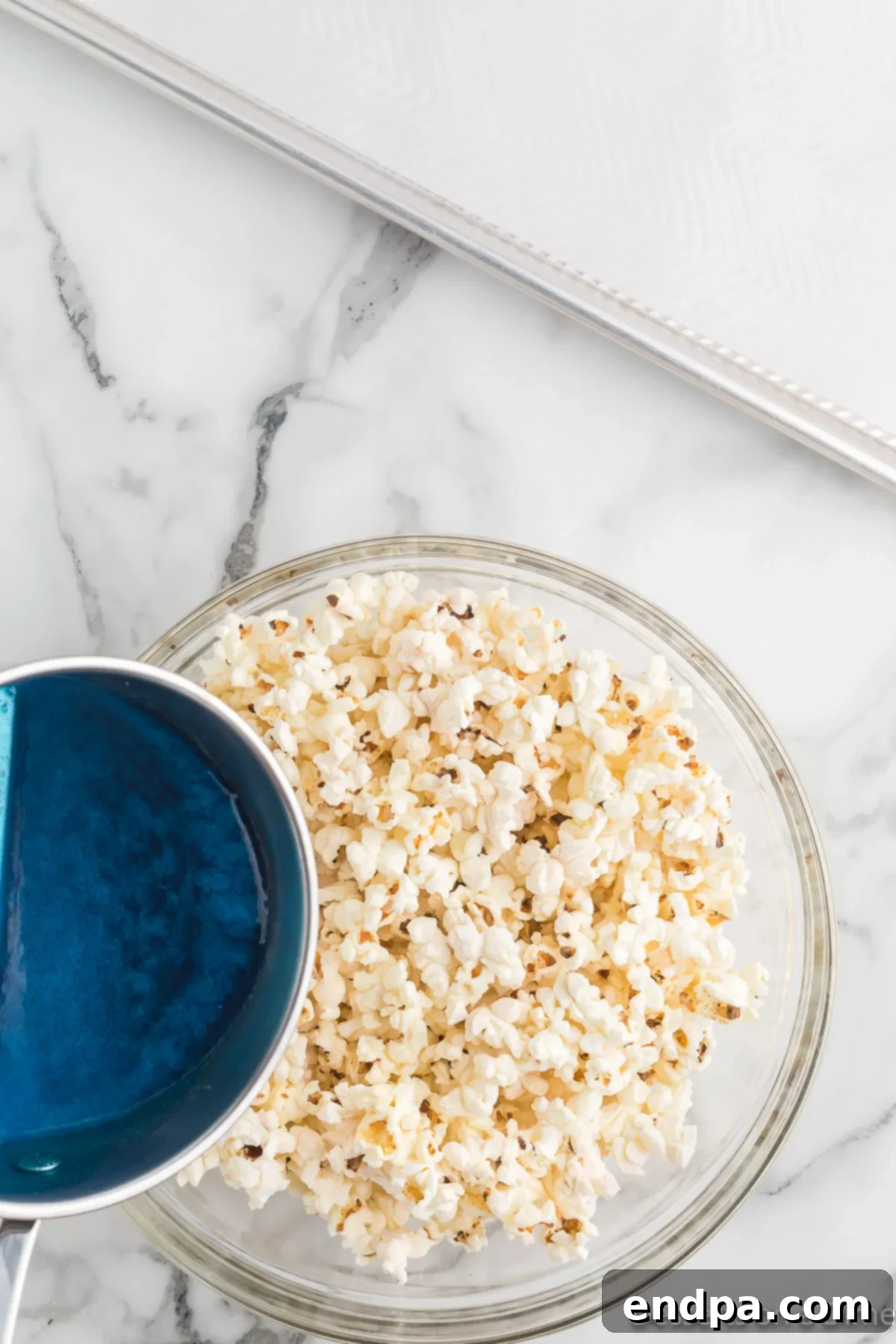 Popped popcorn in a large bowl with the brightly colored candy mixture ready to be poured over it.
