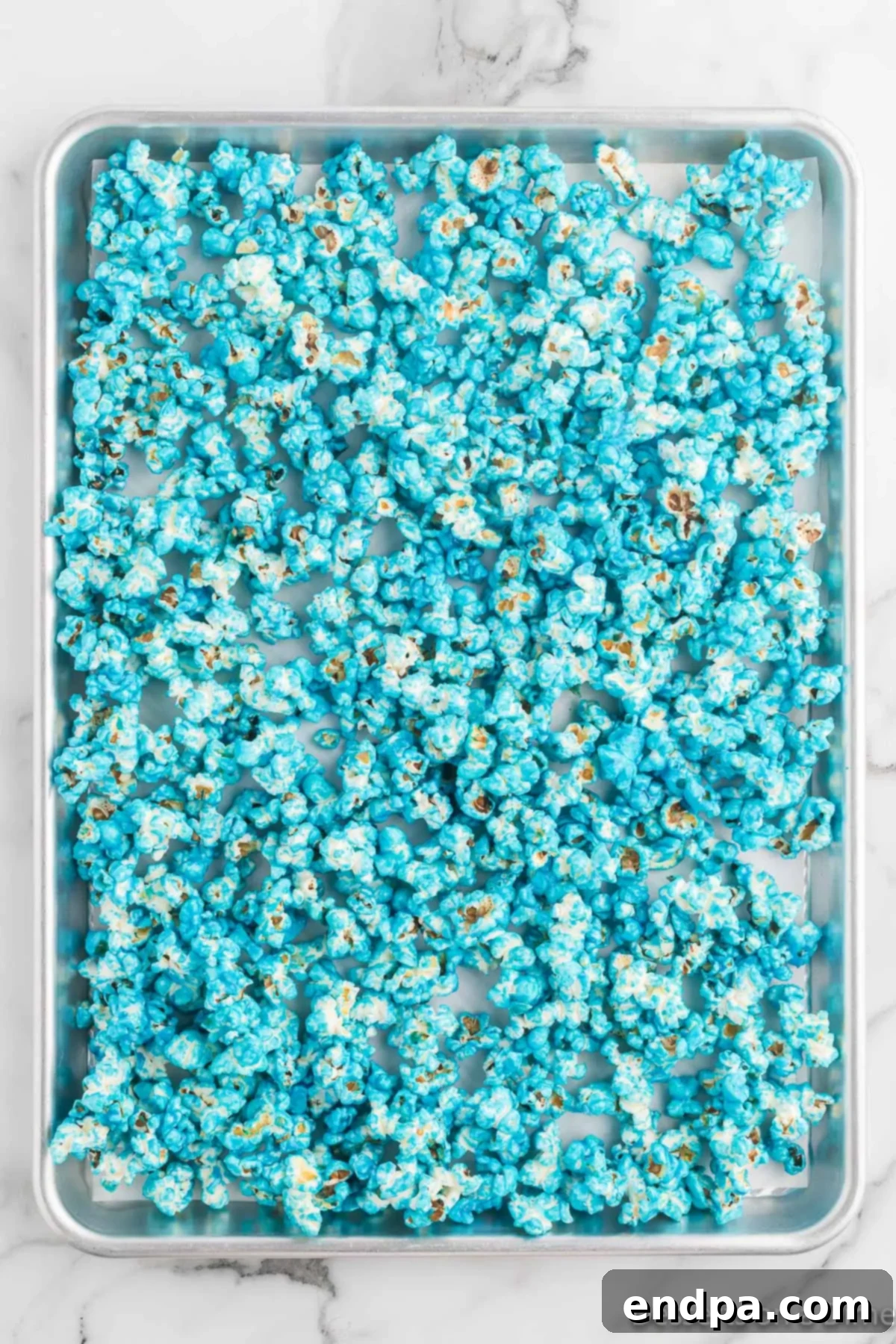 Coated popcorn spread thinly on a baking sheet to cool and set, showing its even blue color.