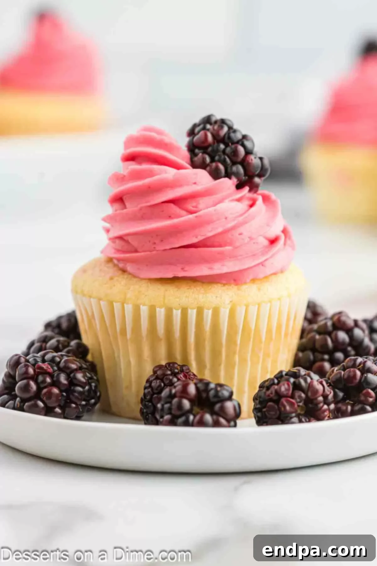 Multiple cupcakes topped with swirled Blackberry Buttercream Frosting, garnished with fresh blackberries, presented beautifully.