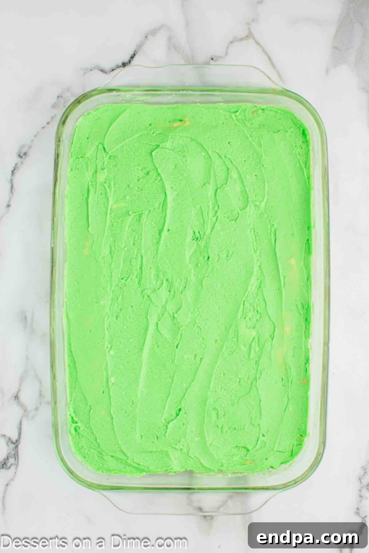 Smooth green frosting being evenly spread across the top of the cooled Grinch cookie bars.