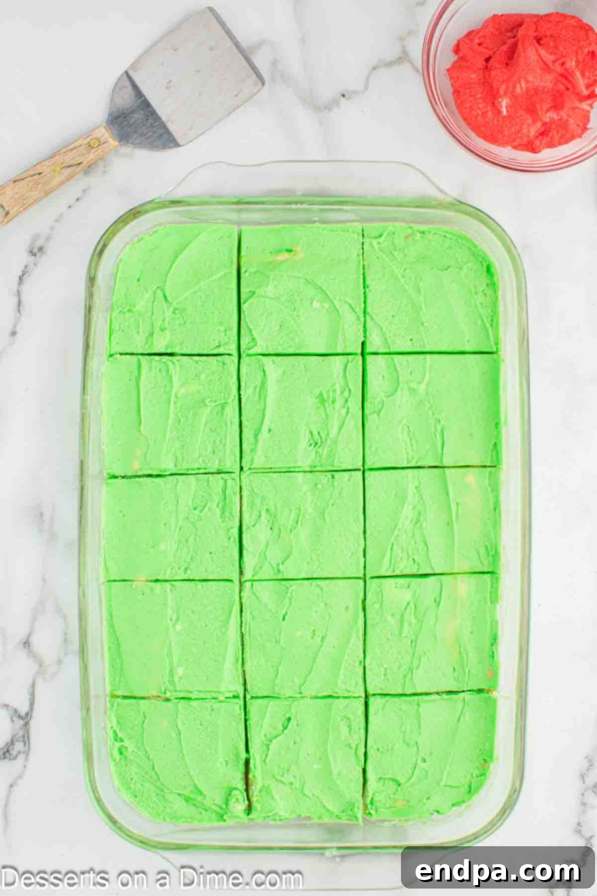 Grinch Cookie Bars, frosted green and decorated with red hearts, neatly cut into individual squares.