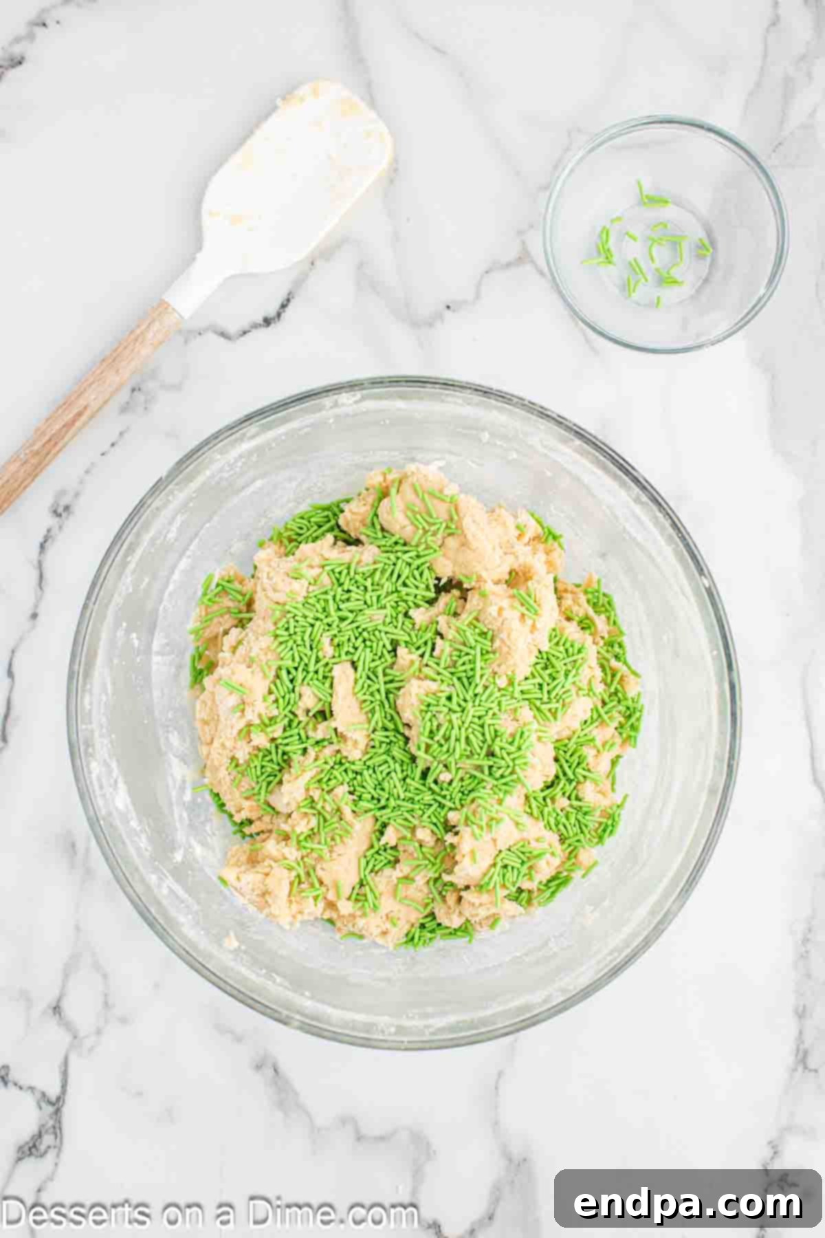 Bright green jimmie sprinkles being folded carefully into the prepared cookie dough.