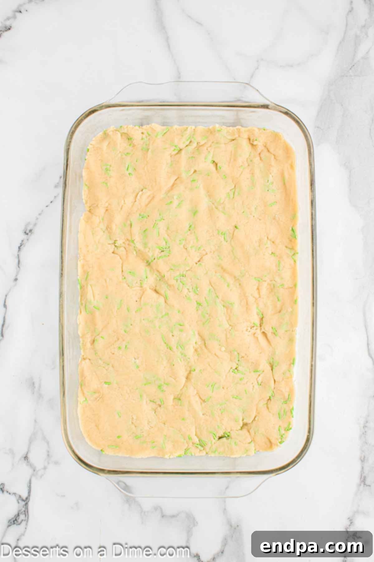 Cookie dough being pressed firmly and evenly into the prepared 9x13 inch baking dish.