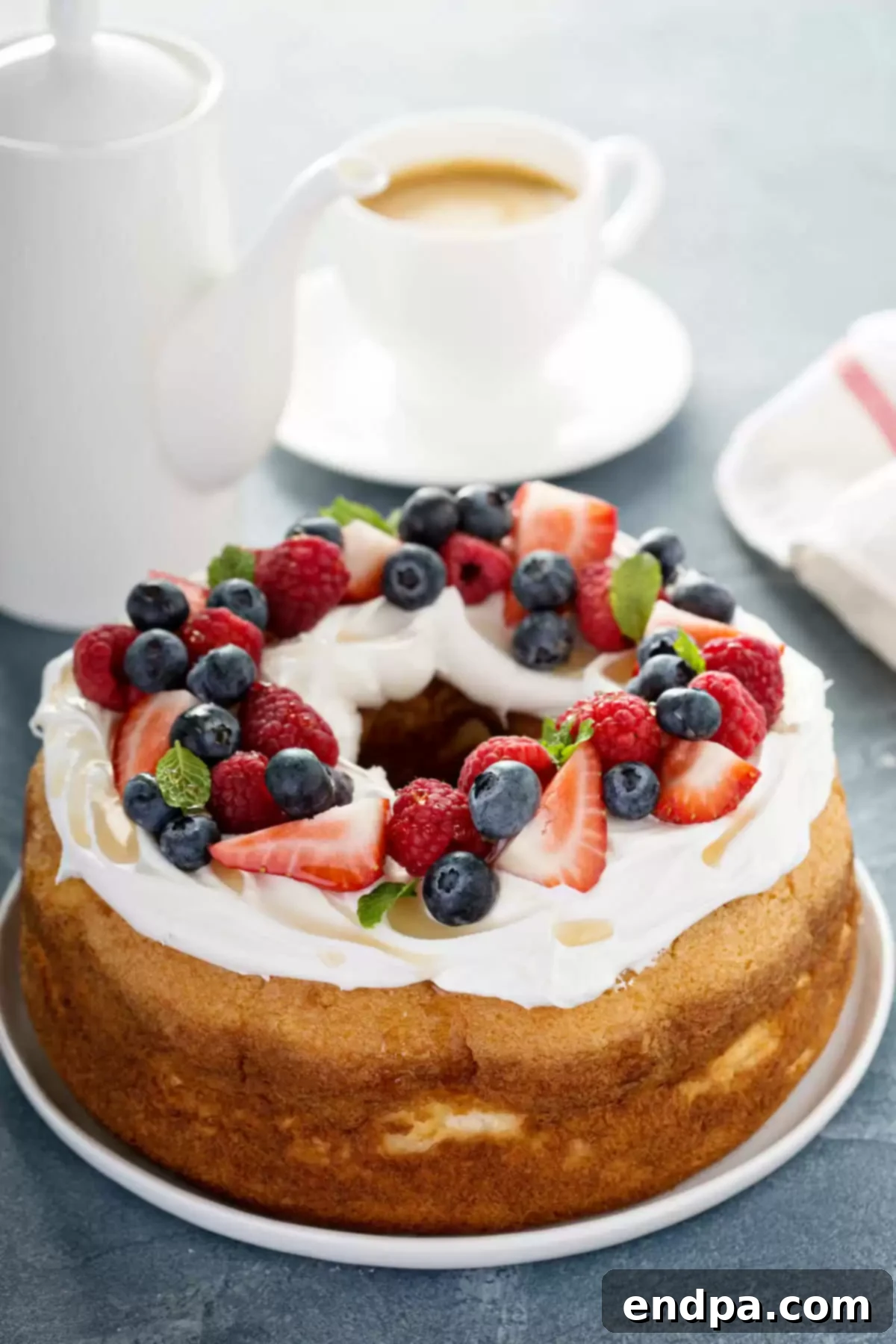 A beautifully presented angel food cake on a platter, adorned with an assortment of fresh berries and a light dusting of powdered sugar, ready to be enjoyed or stored.