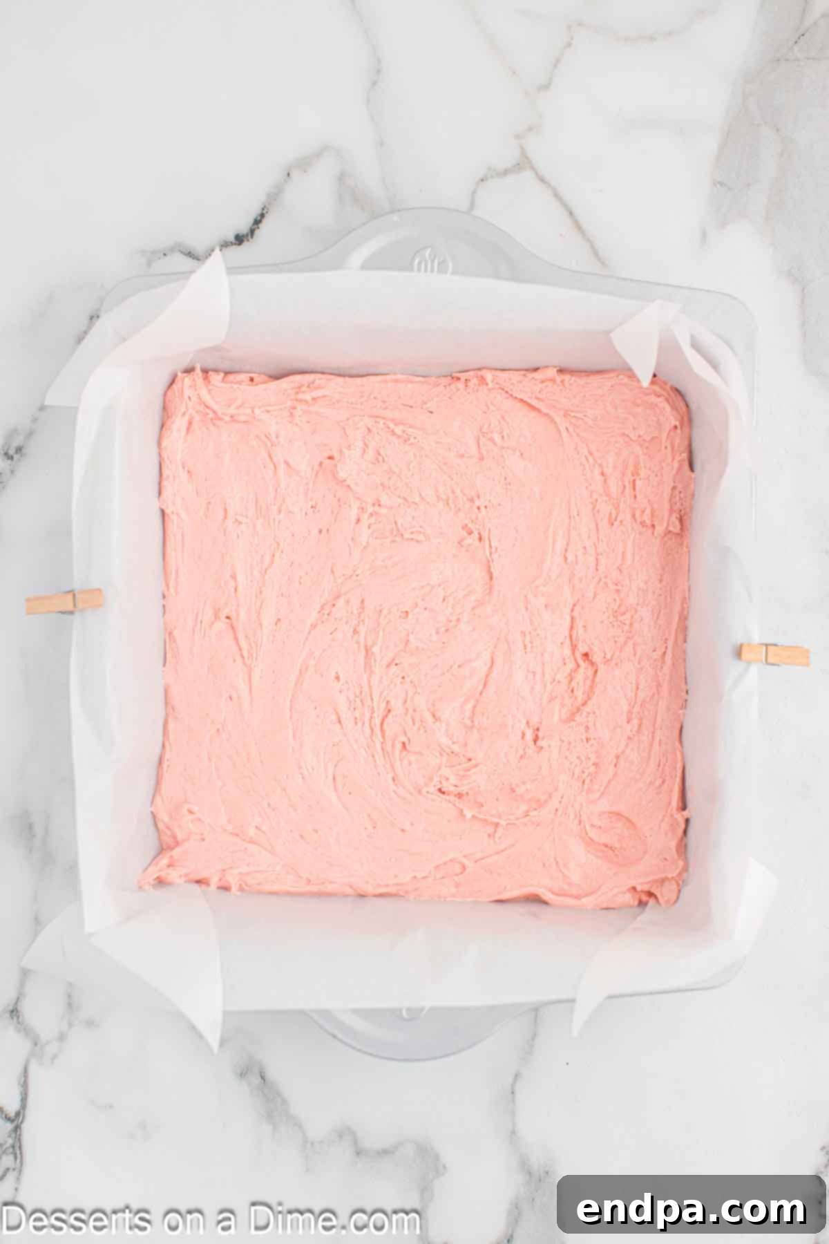 Thick strawberry brownie batter spread evenly into a parchment-lined baking pan, ready for the oven.