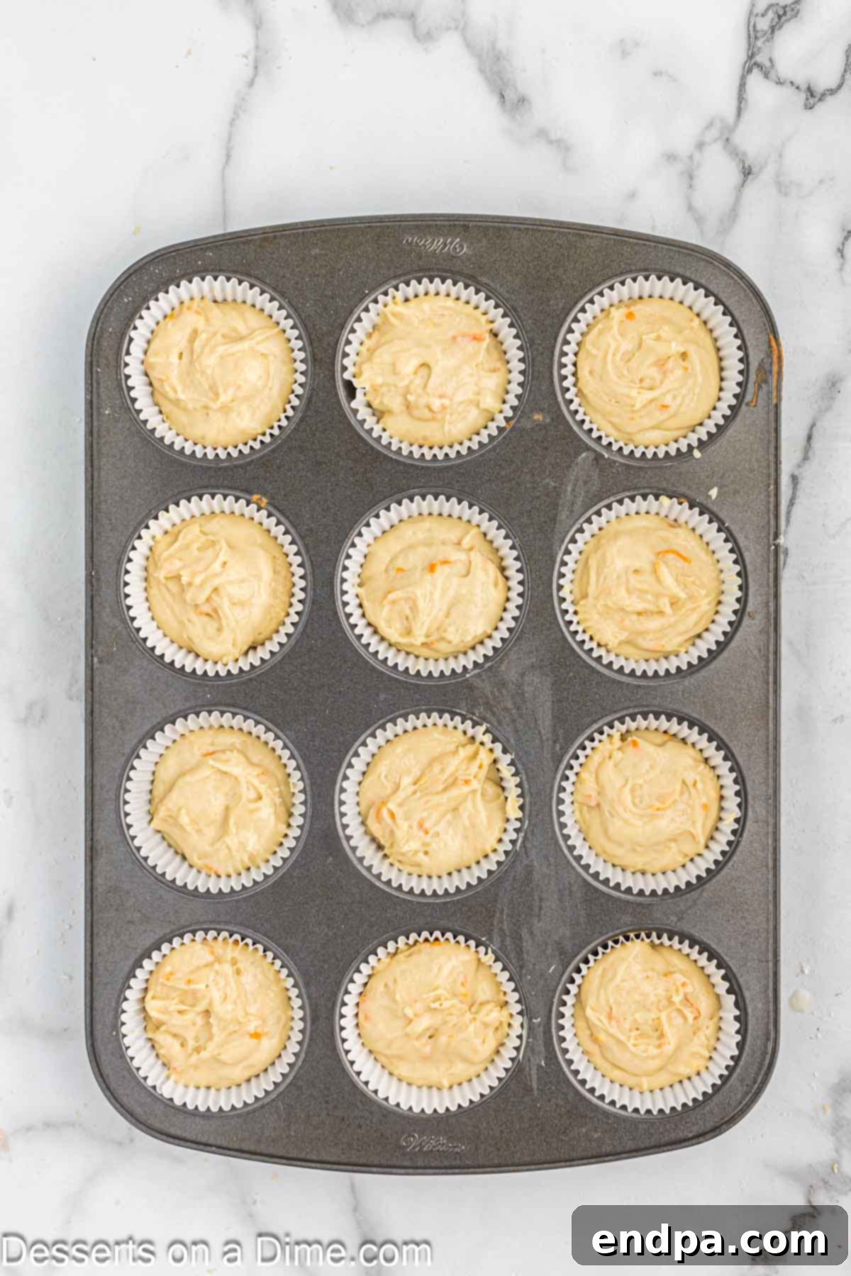 Cupcake liners in a muffin pan, filled with smooth orange-infused batter, ready for baking.