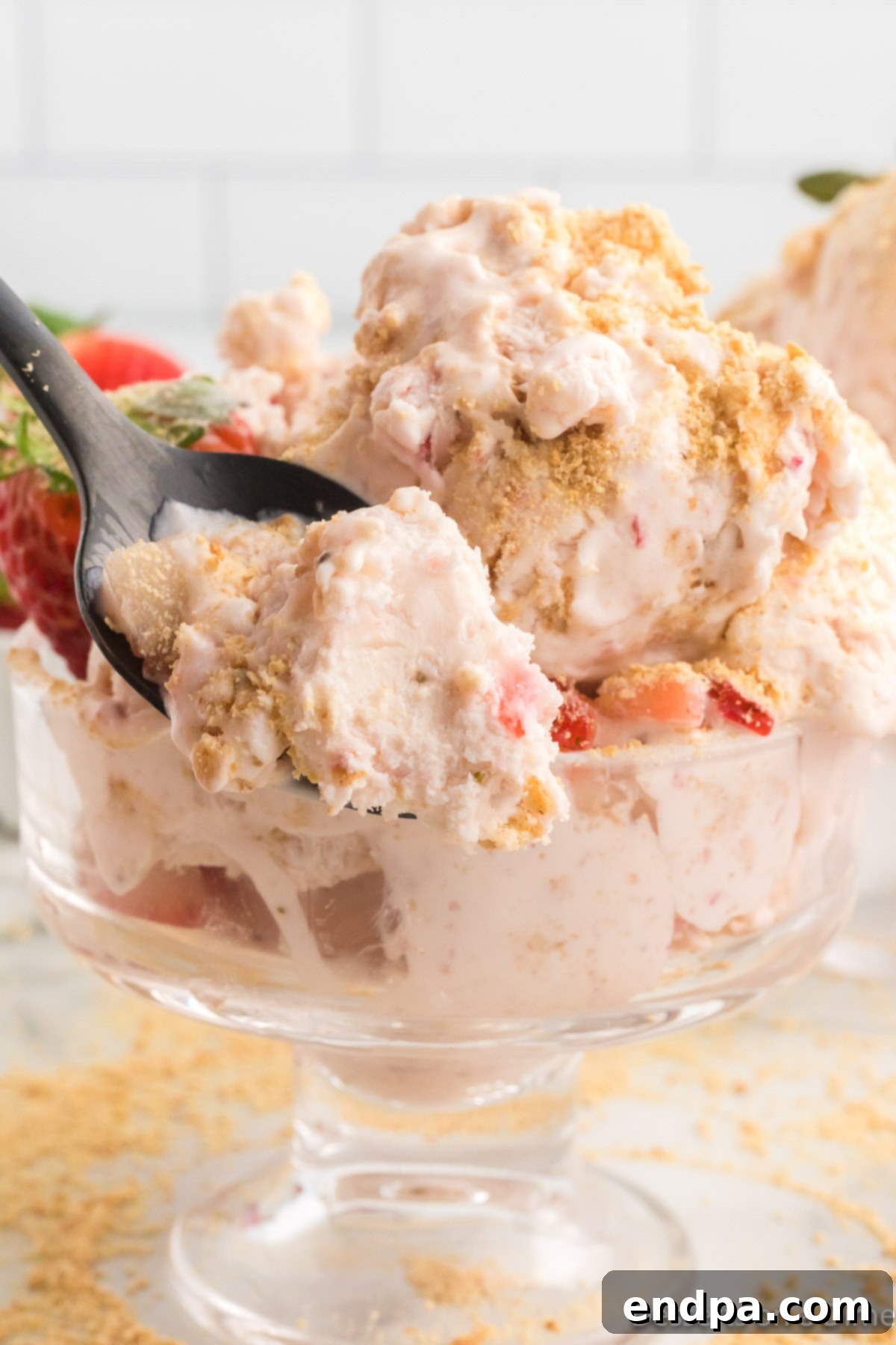 A scoop of homemade Strawberry Cheesecake Ice Cream in a bowl, garnished with fresh strawberries and graham cracker crumbs.