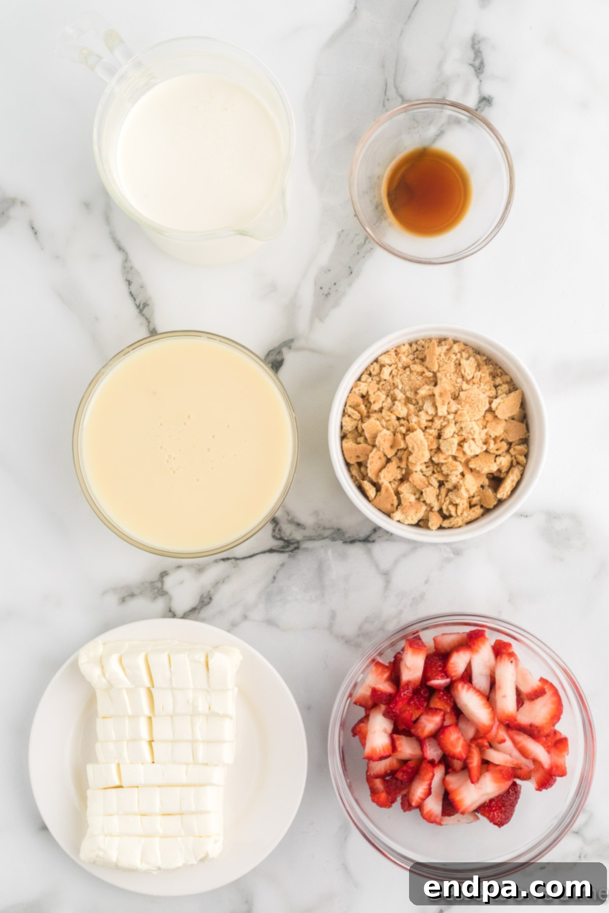 A flat lay of ingredients for Strawberry Cheesecake Ice Cream: sliced fresh strawberries, a can of sweetened condensed milk, heavy cream, vanilla extract, a block of cream cheese, and graham crackers.