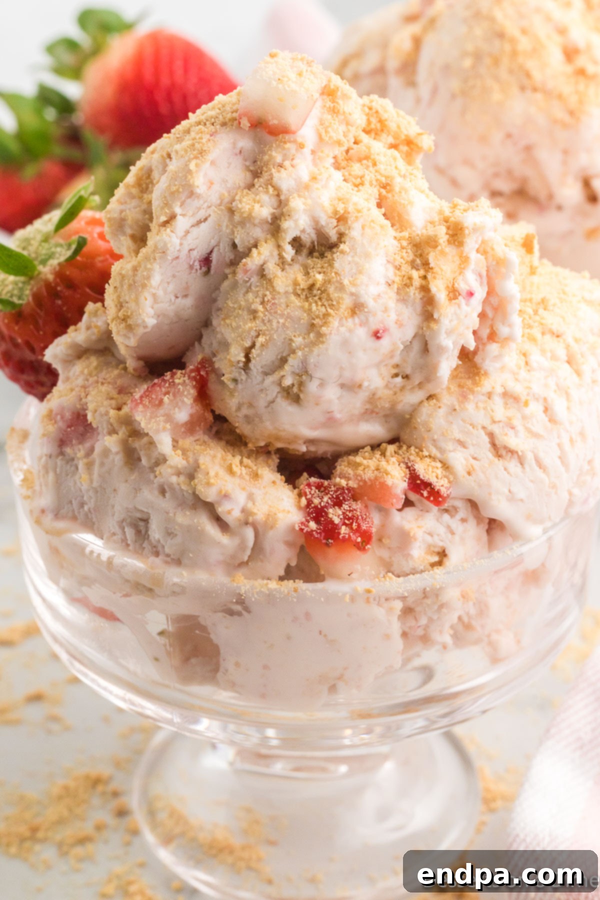 A close-up shot of creamy Strawberry Cheesecake Ice Cream in a bowl, with visible strawberry pieces and graham cracker crumbs.