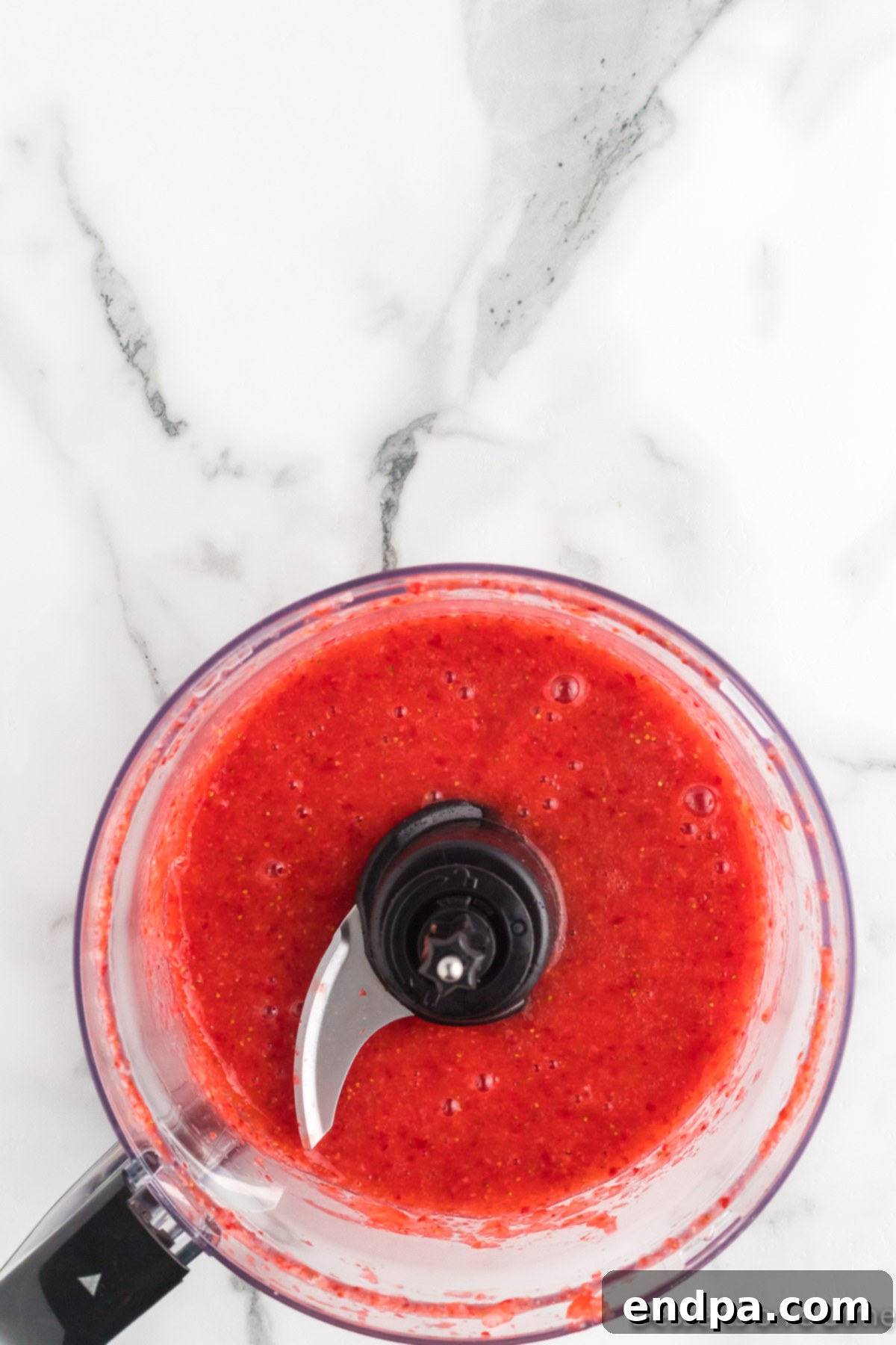 Pureed strawberries in a food processor, a vibrant red liquid.