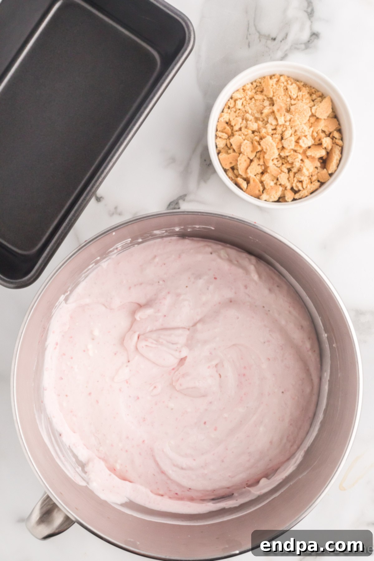 Diced cream cheese and strawberry puree being gently folded into the whipped cream mixture in a bowl.