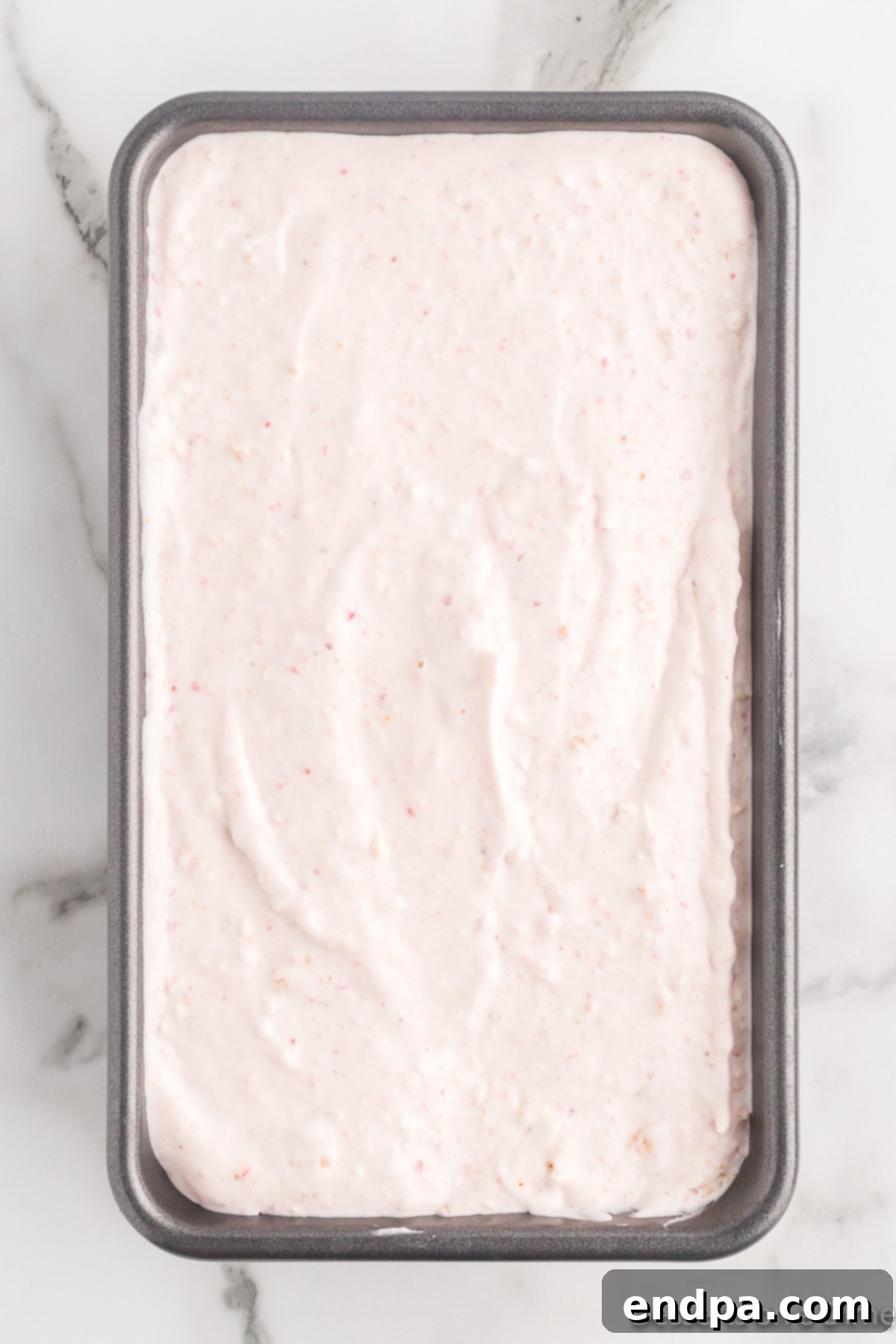 Crushed graham crackers being folded into the ice cream mixture, which is then poured into a loaf pan.