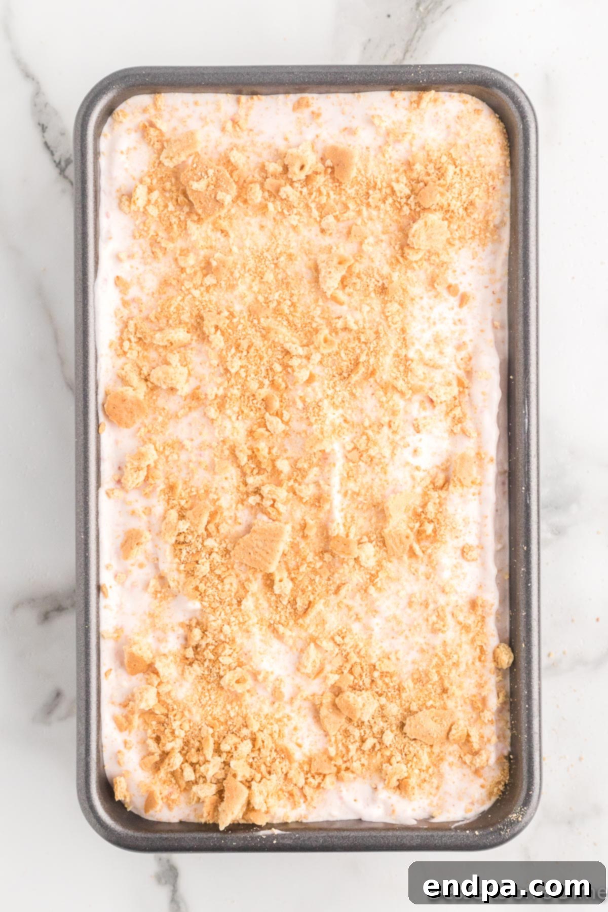 The ice cream mixture in a loaf pan, with remaining graham cracker crumbs sprinkled on top.