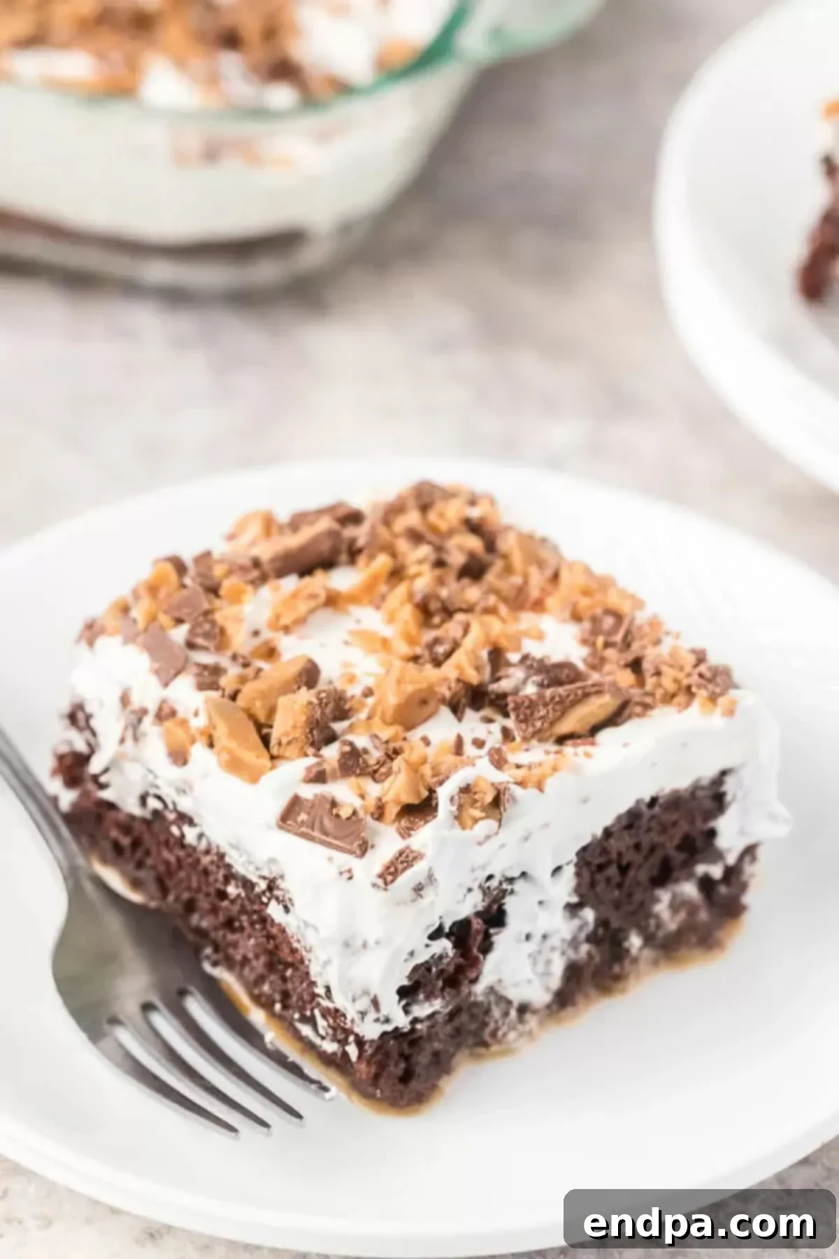 Better than sex cake recipe is so decadent! It's also known as heath bar cake recipe and each bite is loaded with caramel, chocolate, toffee and more. Heath bar cake recipe desserts are so easy and chocolate heath bar cake is a must try. Heath bar cake condensed milk and other simple ingredients make such an easy heath bar cake. #dessertonadime #betterthansexcakerecipe A slice of better than sex cake on a white plate with a fork.