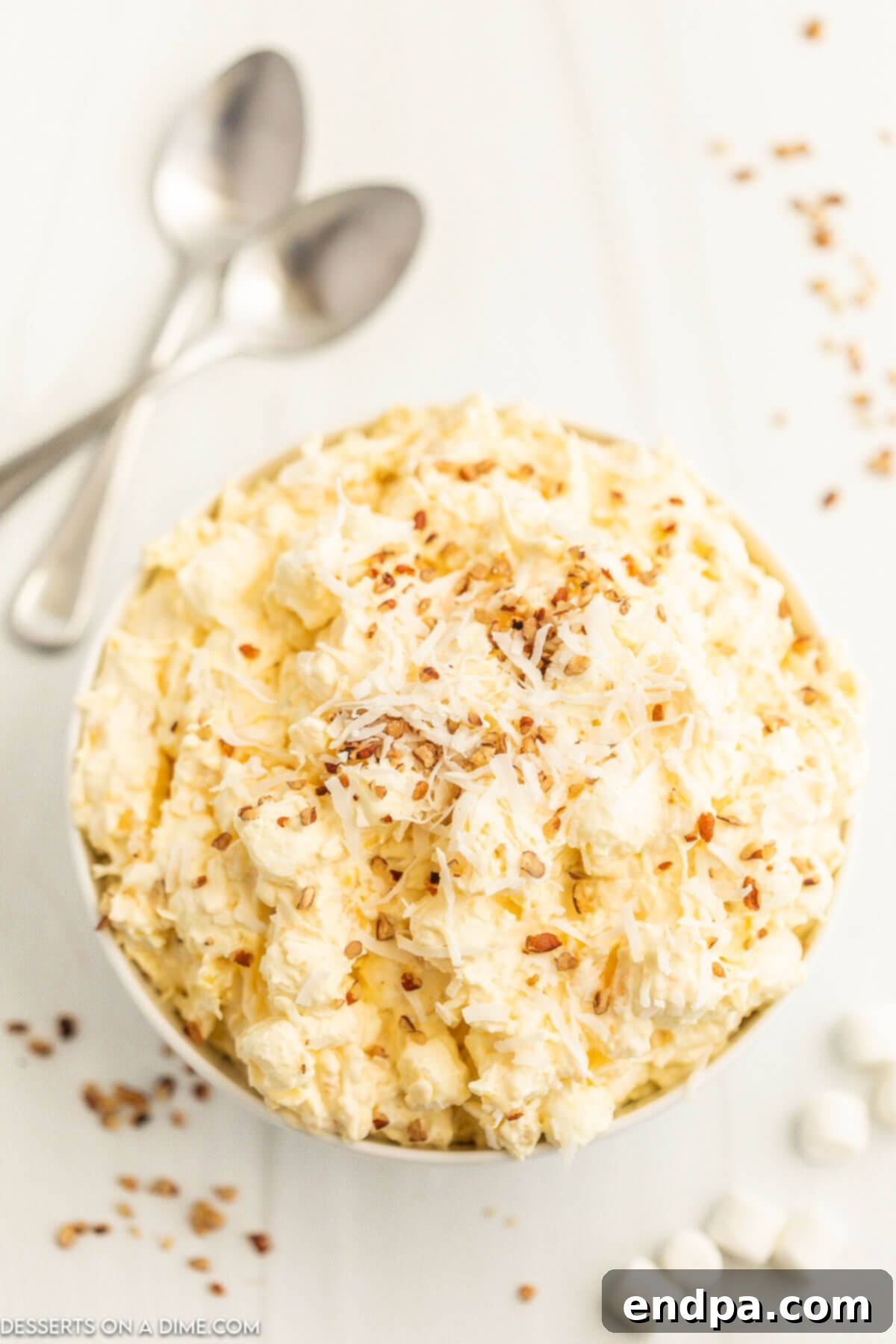 Tropical Pineapple Dream 8 A close-up shot of a bowl of Pineapple Fluff, garnished with toasted coconut and chopped pecans, highlighting its creamy and inviting texture.